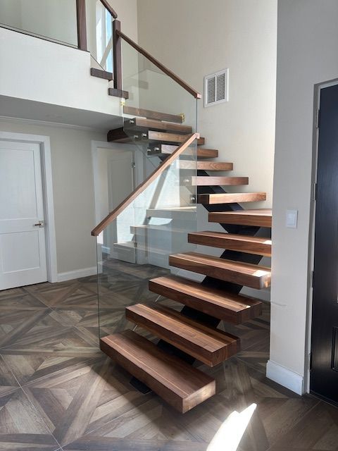 Floating wooden staircase with glass railing.  Interior view, leading to an upper level.