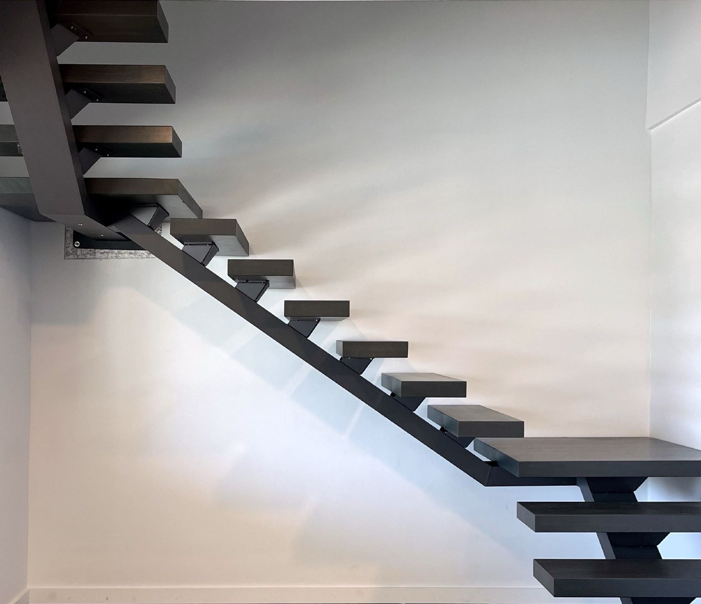 Dark gray floating staircase against a white wall.