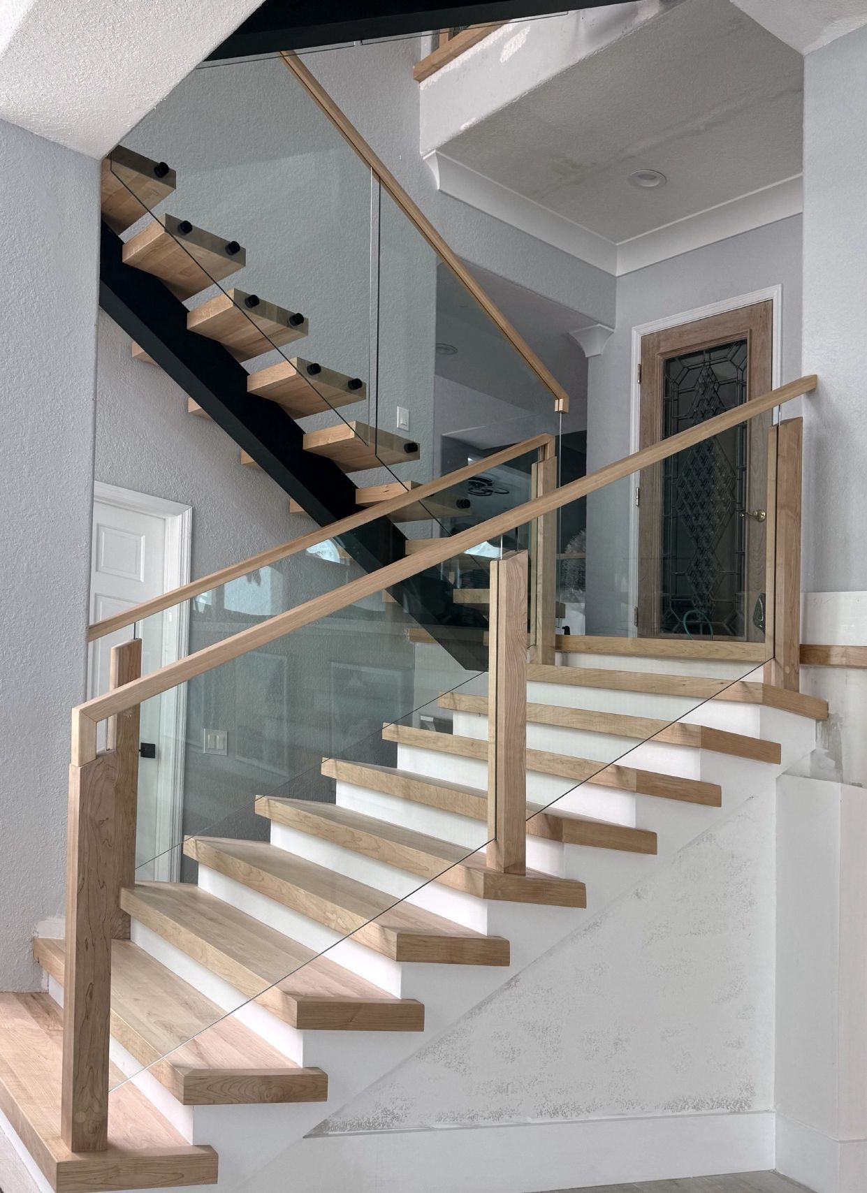 Modern staircase with wooden treads, glass railing, and light wood banister.