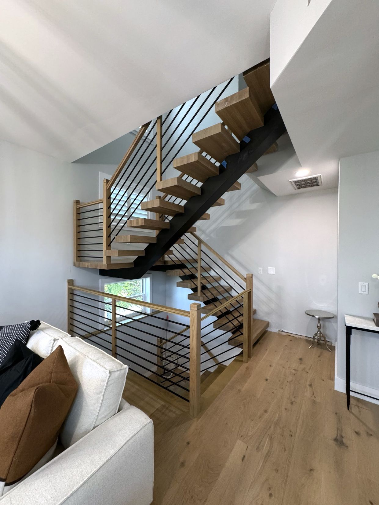 Modern wooden staircase with black metal railings, leading to the upper level of a house with light wood flooring.