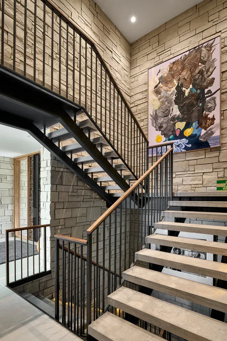 Staircase with concrete steps, black metal railing, and textured stone walls. Large colorful painting on the wall.