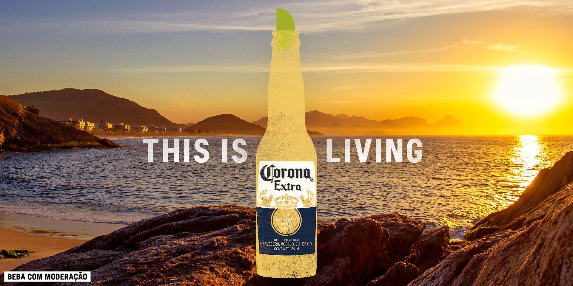 Uma garrafa de cerveja corona está em uma praia rochosa ao pôr do sol