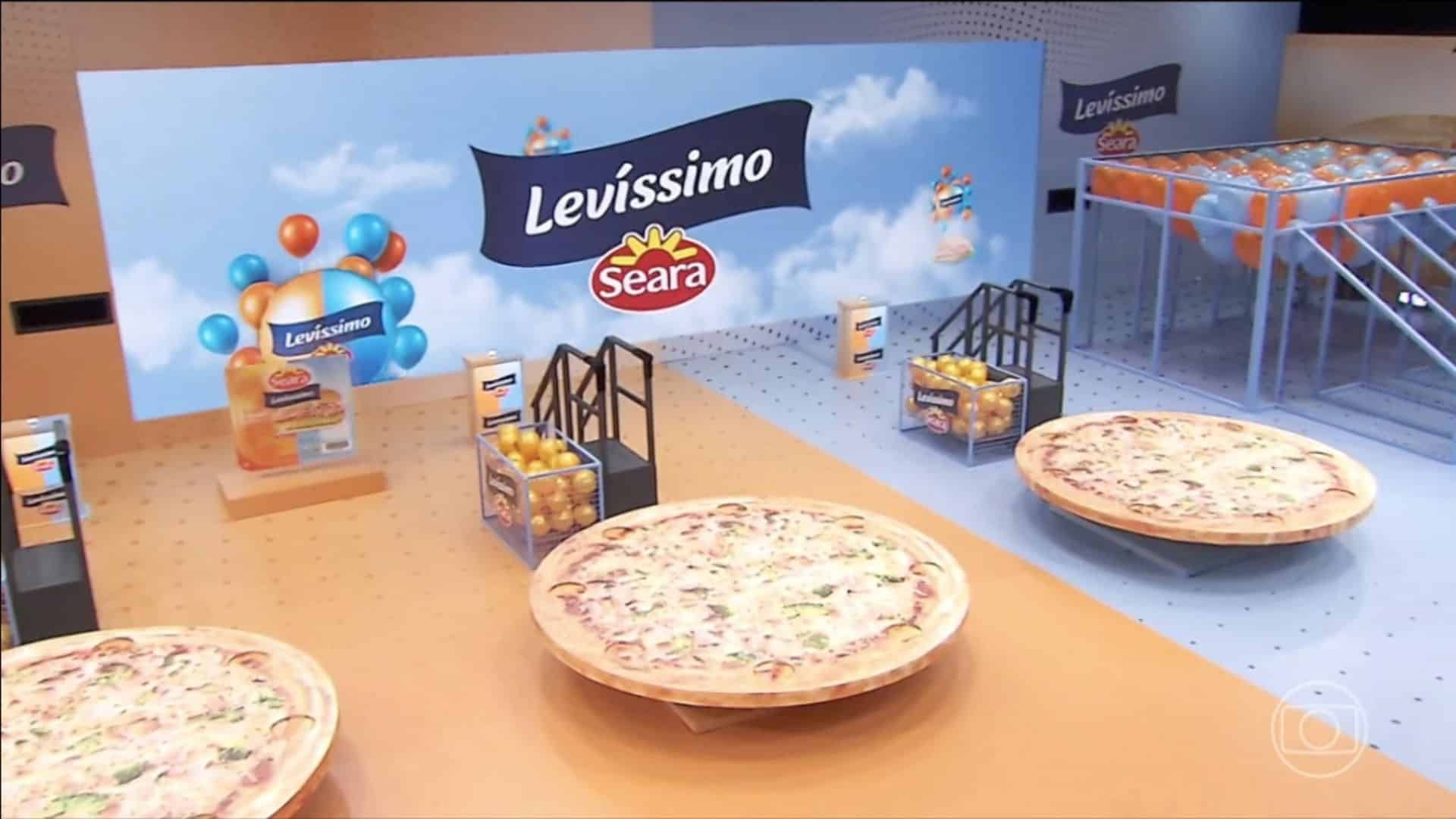 Três pizzas estão sobre uma mesa em frente a uma placa que diz levissimo seara.