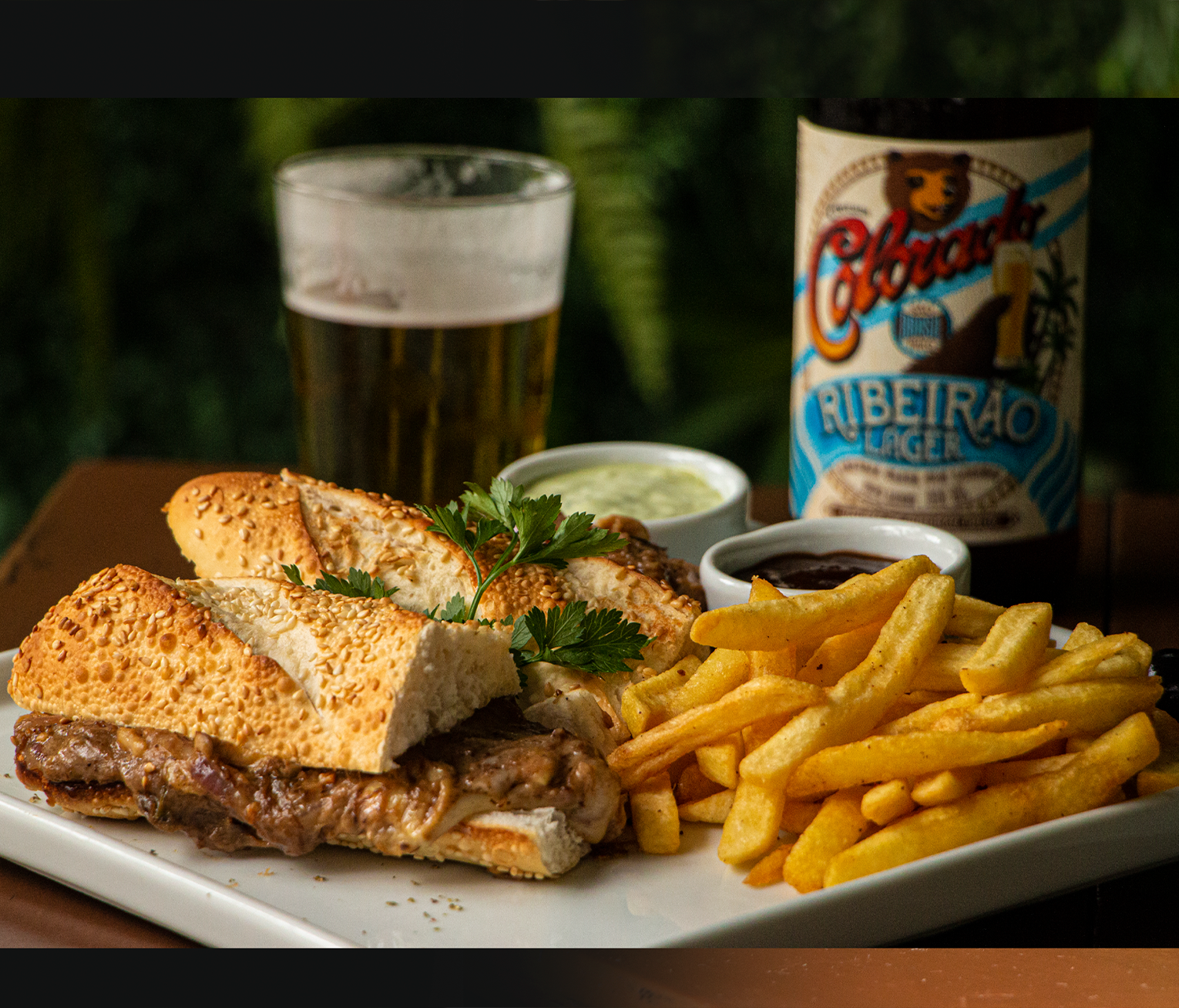 Berton Botequim e Restaurante Um sanduíche e batatas fritas em um prato com uma garrafa de cerveja ao fundo.