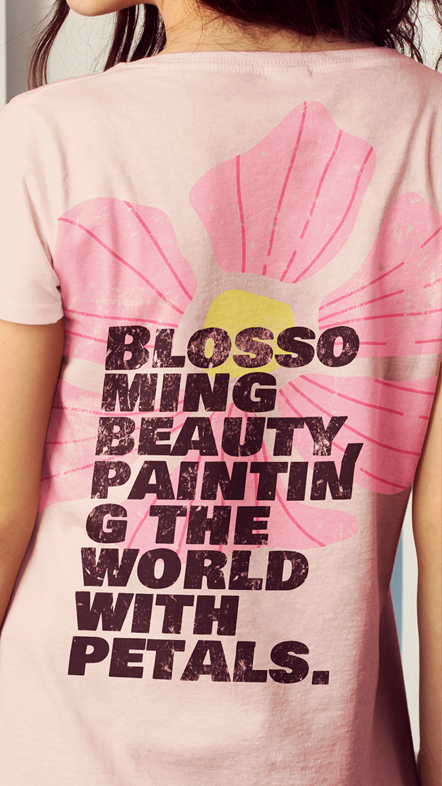 Uma mulher está vestindo uma camiseta rosa que diz beleza de asa de flor pintando o mundo com pétalas.