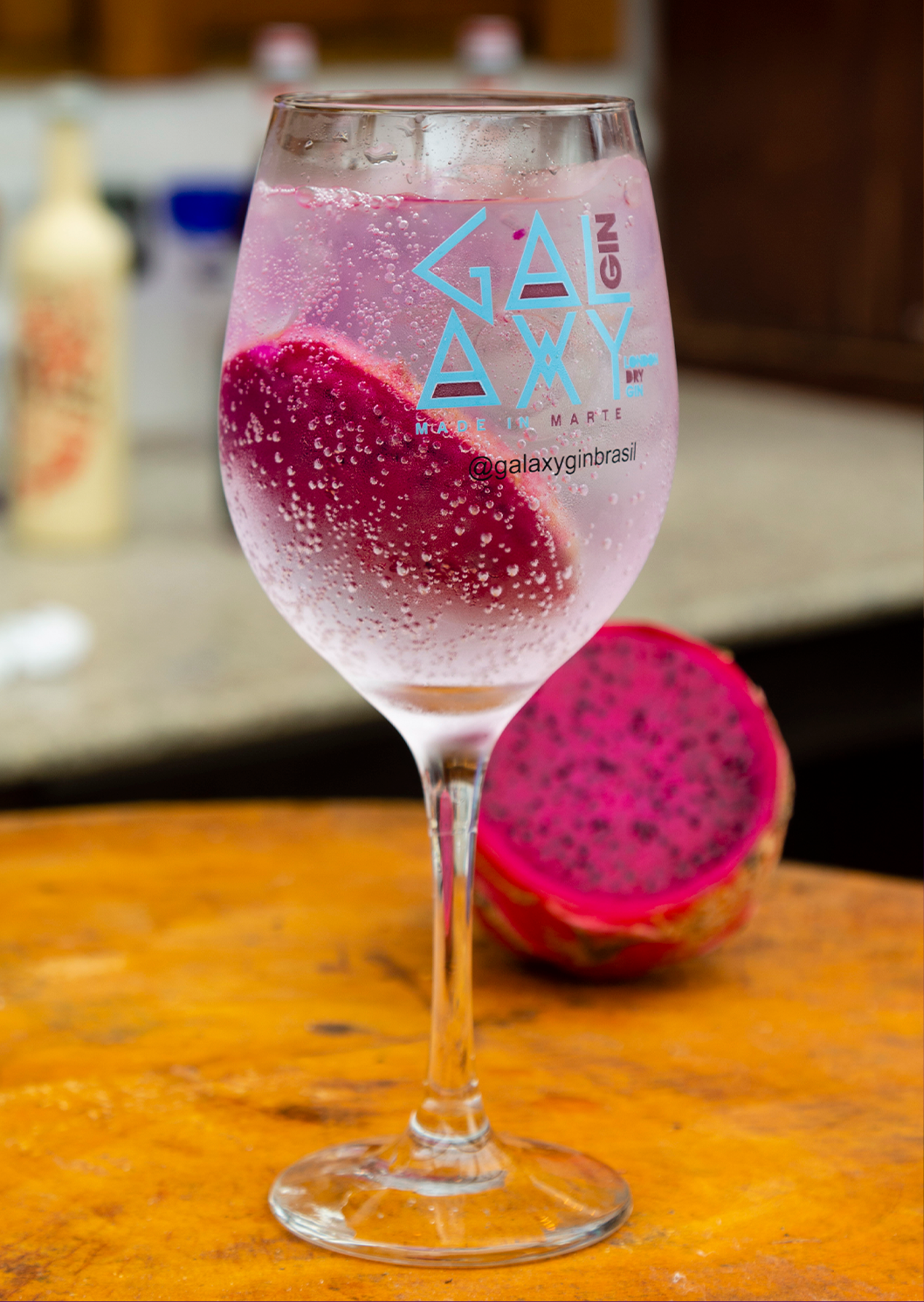 Uma taça de vinho cheia de uma bebida rosa ao lado de uma fatia de pitaia.