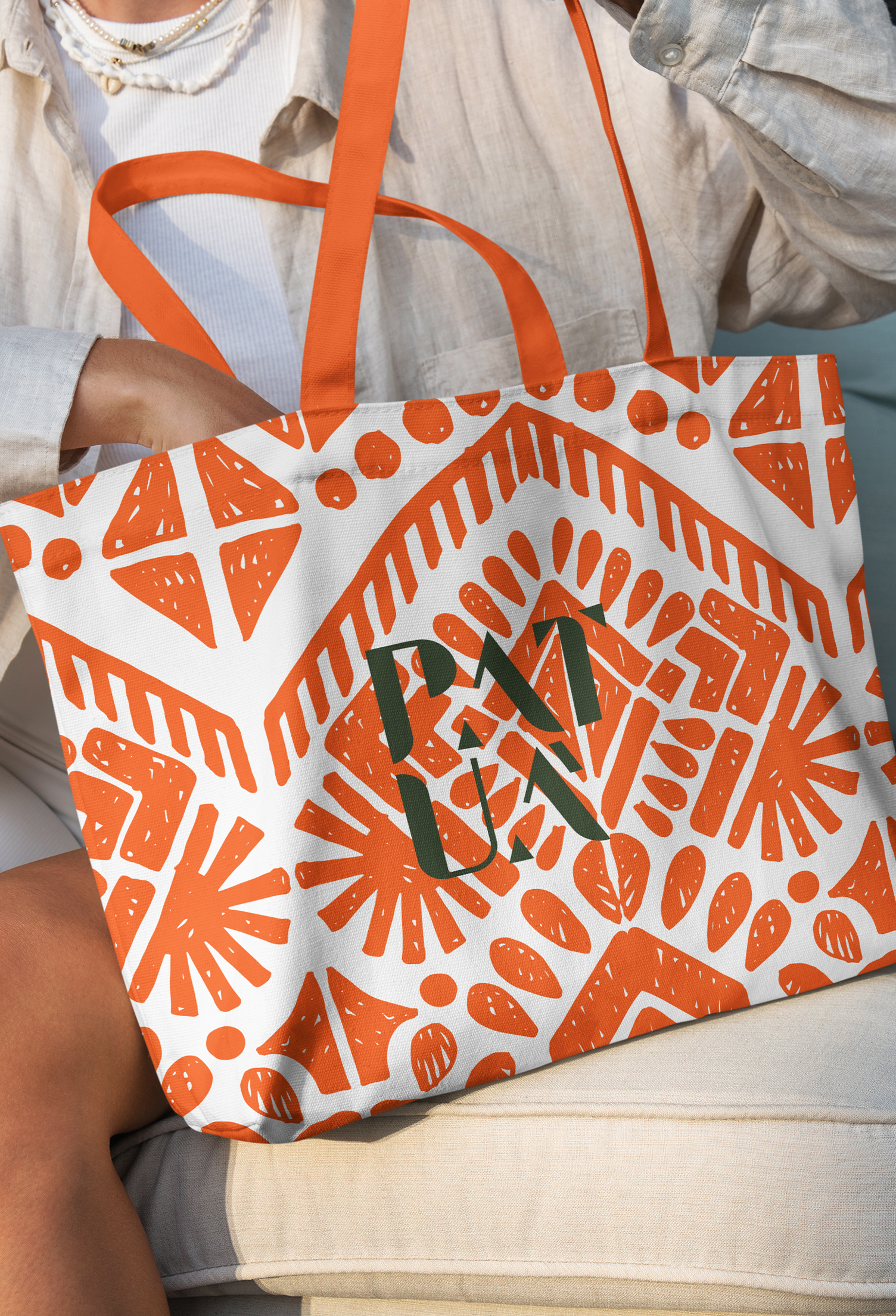 PATUÁ A person is holding an orange and white tote bag with the letter m on it.
