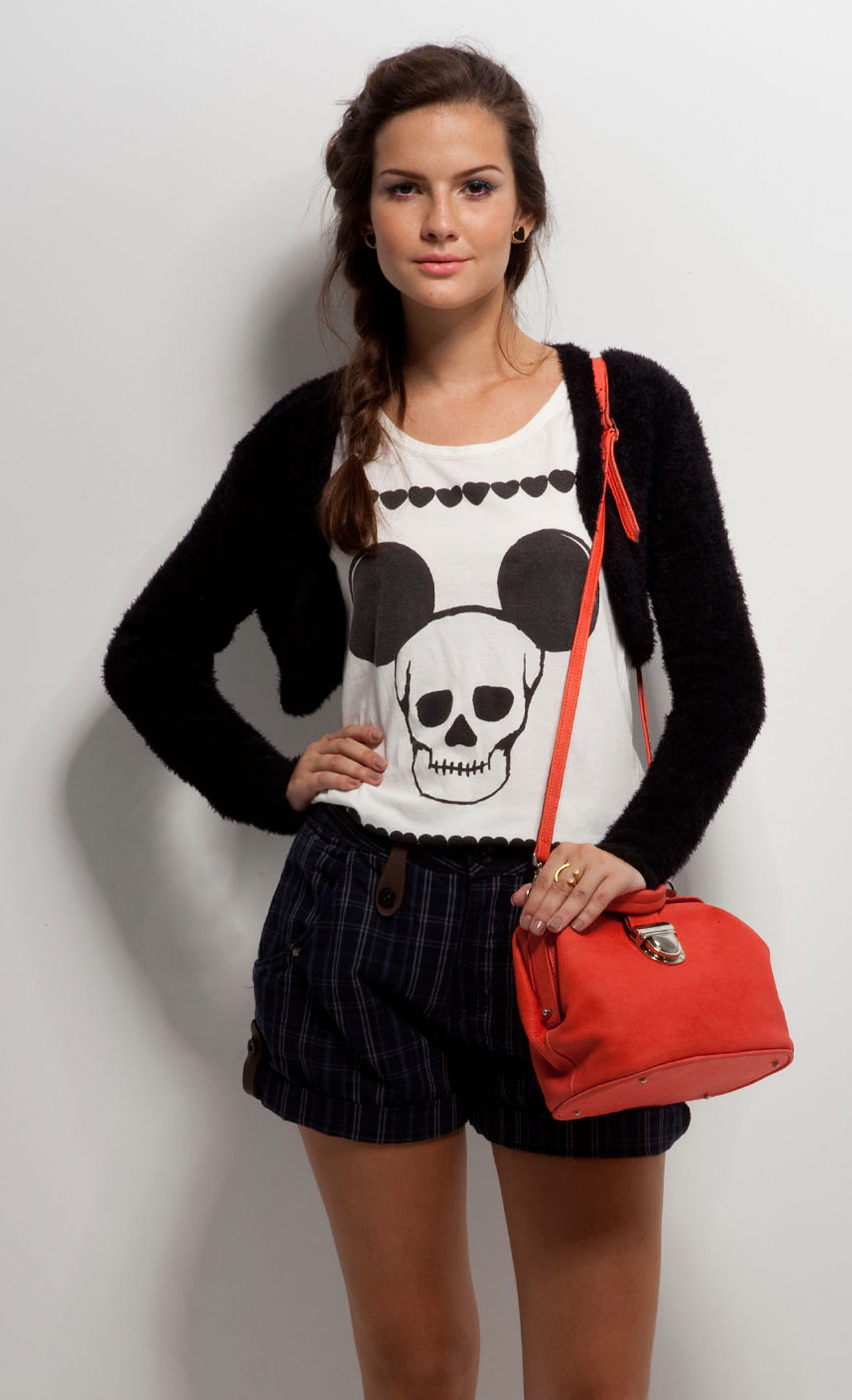 A woman wearing a mickey mouse shirt and shorts is holding a red purse