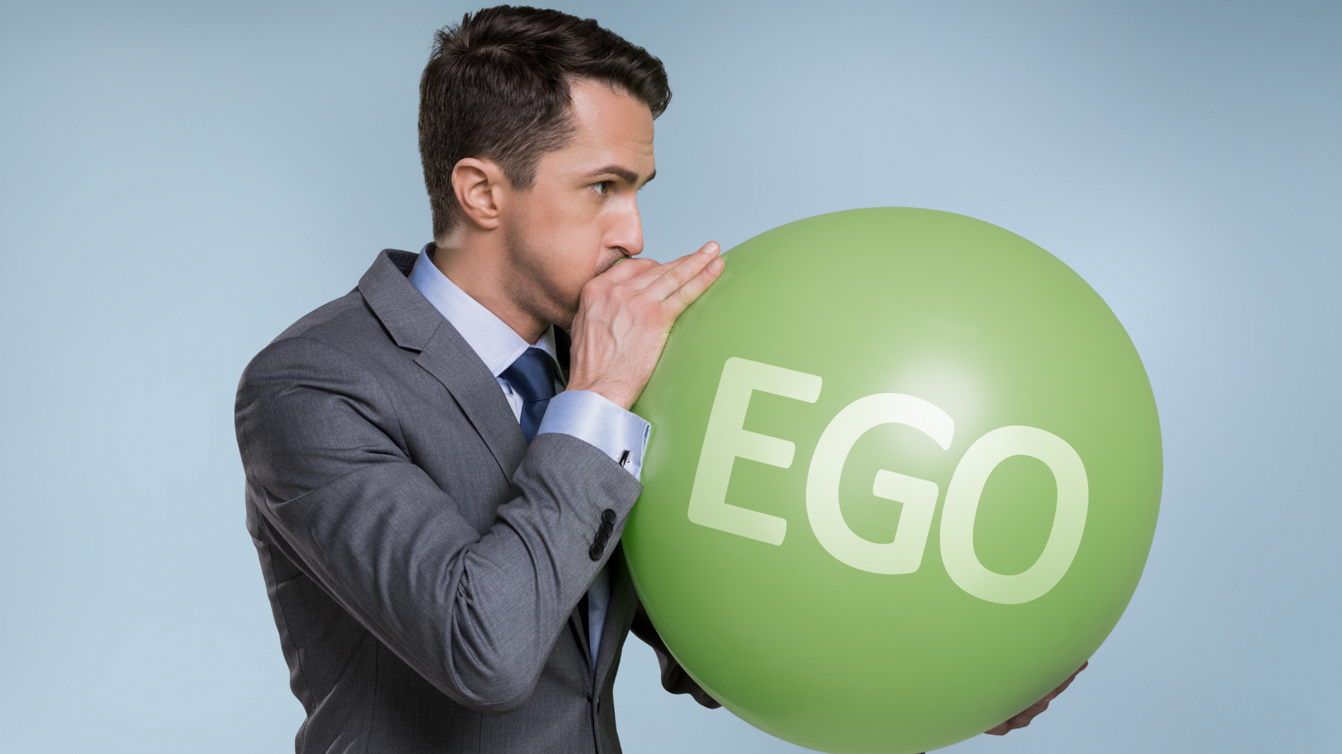 Um homem de terno está enchendo um balão verde com a palavra ego nele.