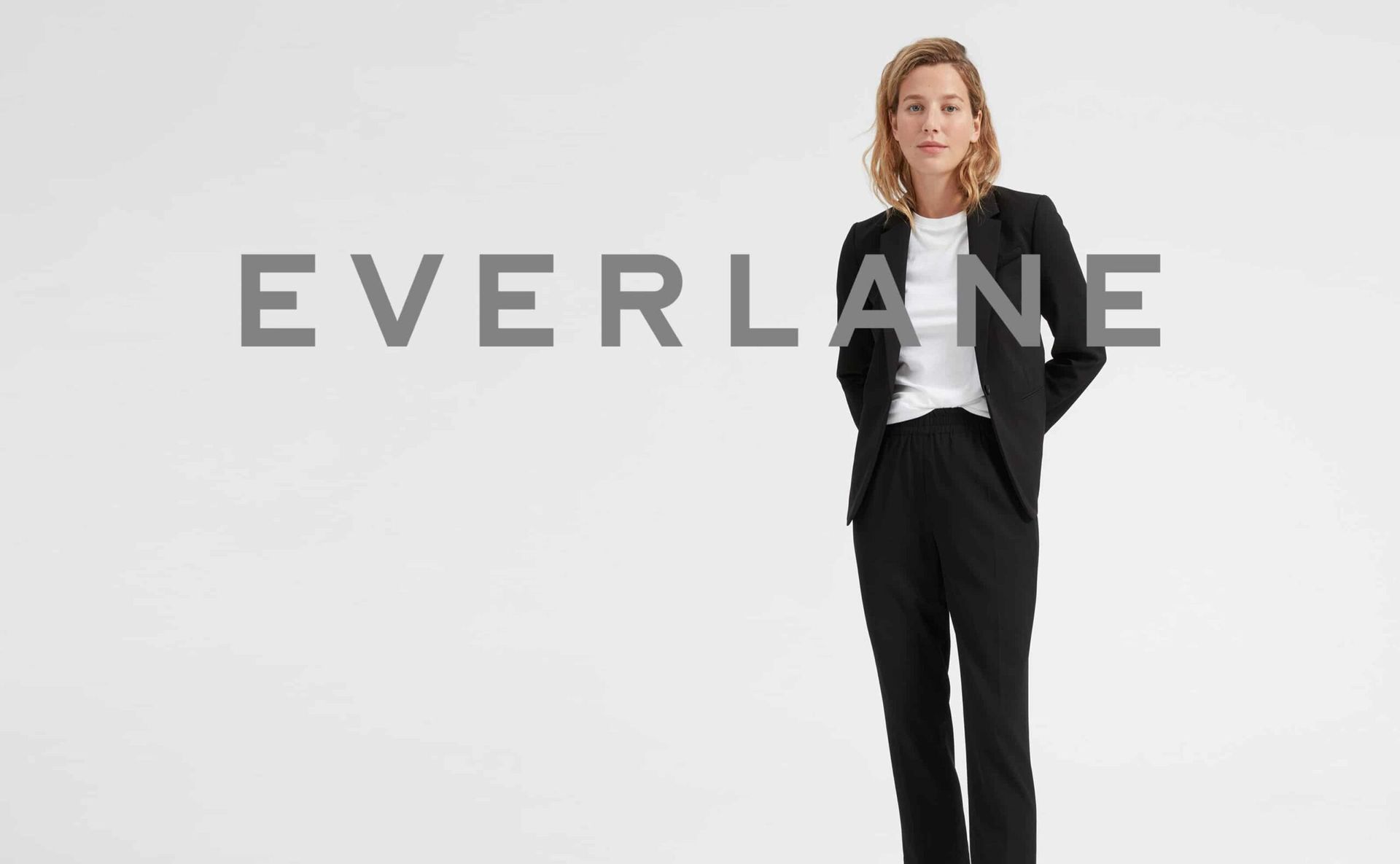 Uma mulher de terno está parada em frente ao logotipo da Everlane.