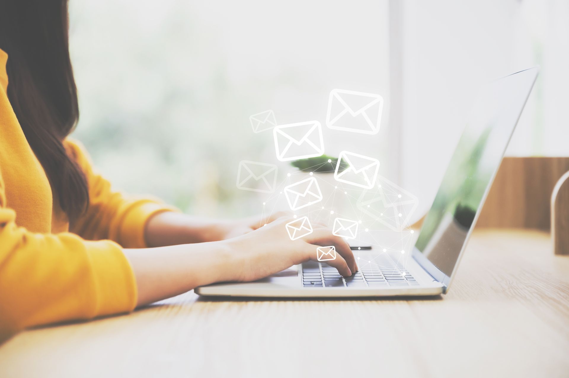 Uma mulher está digitando em um laptop com ícones de envelope saindo da tela.