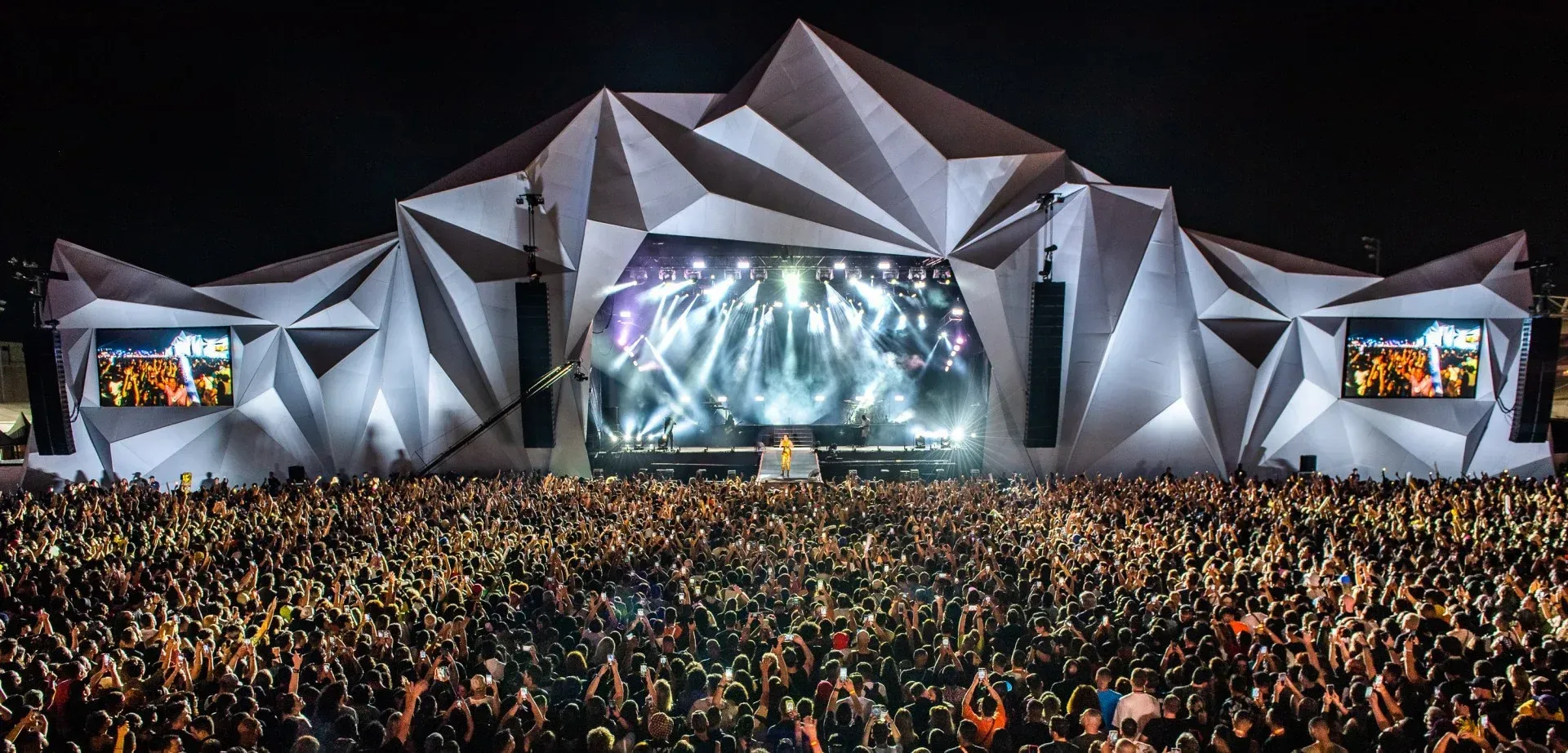Uma grande multidão de pessoas está em frente ao palco de um show.