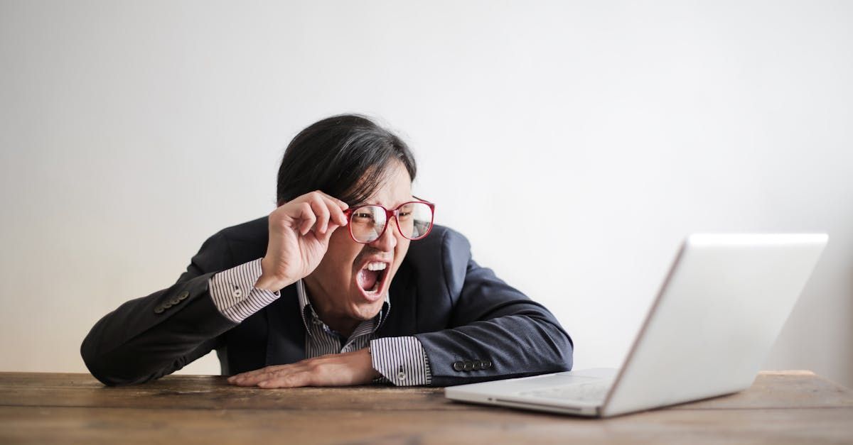 Um homem de óculos está sentado em uma mesa em frente a um laptop.