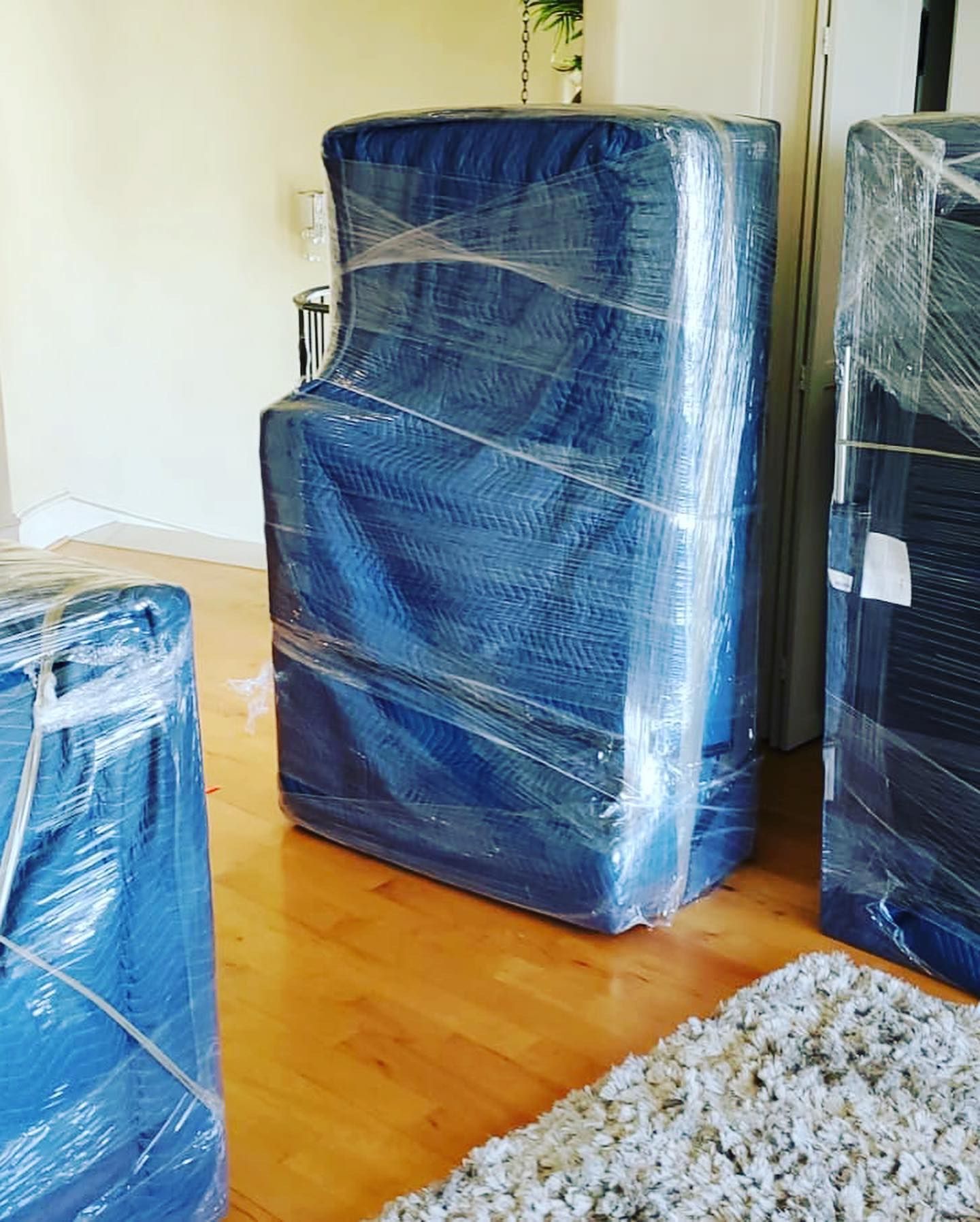 Furniture wrapped in blue moving blankets and plastic wrap, ready to be moved on a hardwood floor.