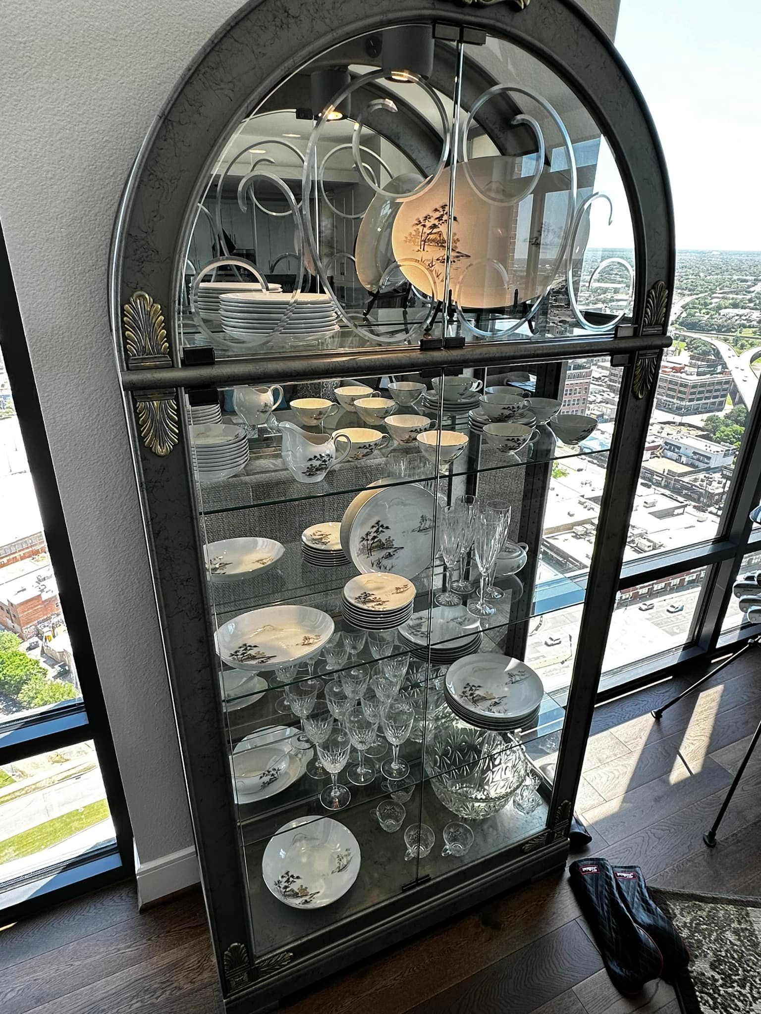 A tall, arched china cabinet filled with white and blue porcelain dishes, reflecting surrounding cityscape.