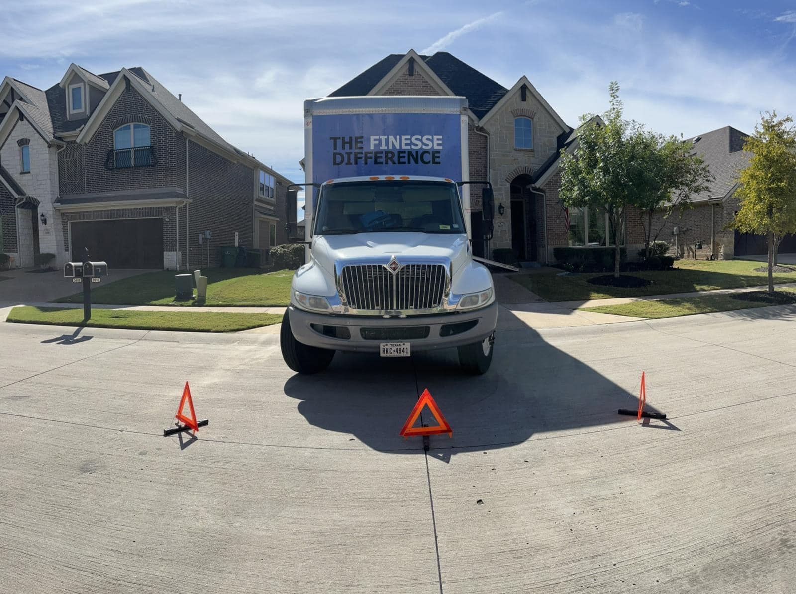 Moving truck parked on a residential street with three orange traffic cones in front.
