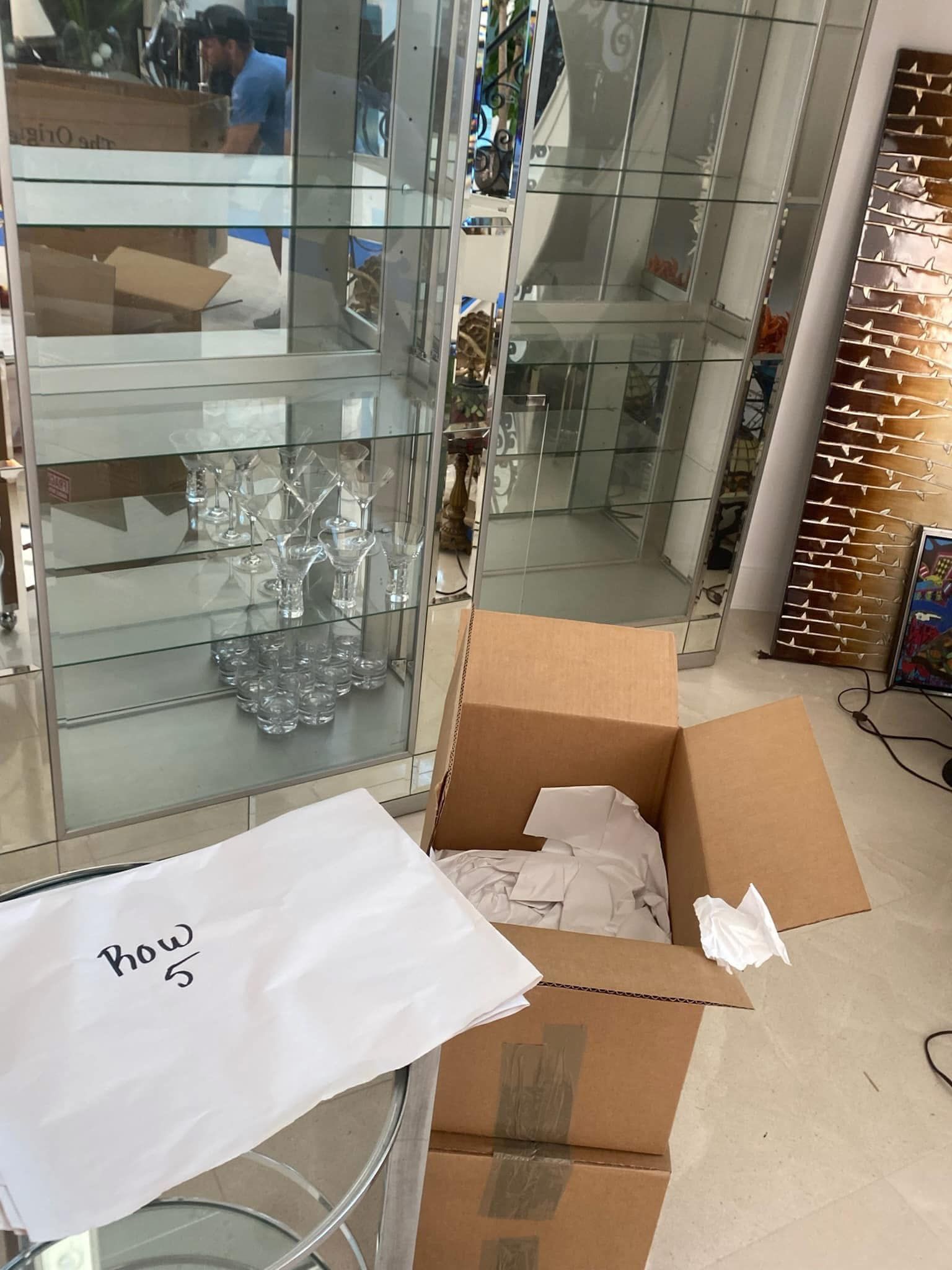 Cardboard box, glass display cabinets, white packaging. Person reflected in cabinet.