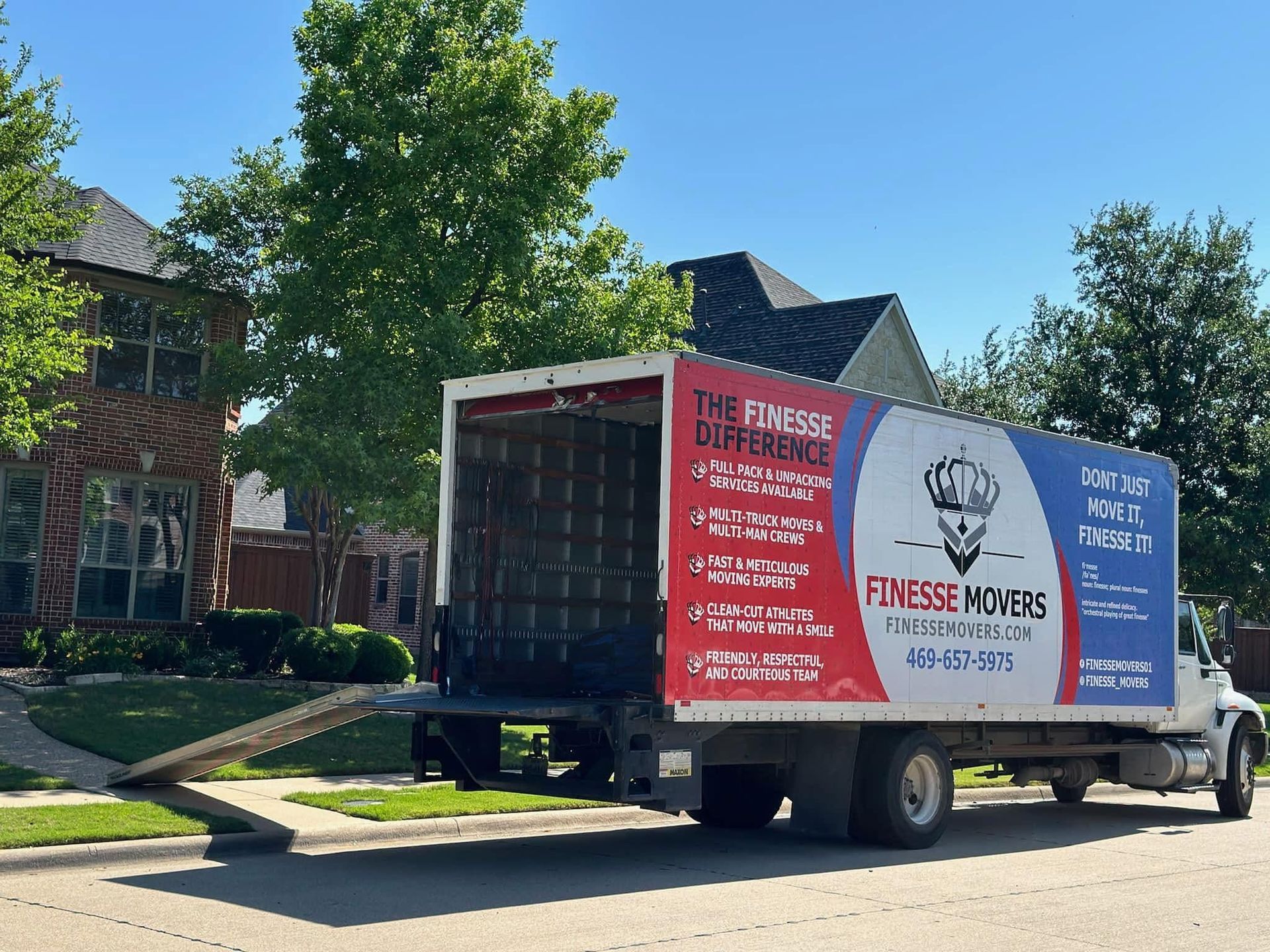 Moving truck parked in front of a house, ramp down. Red, blue, and white signage on the truck.