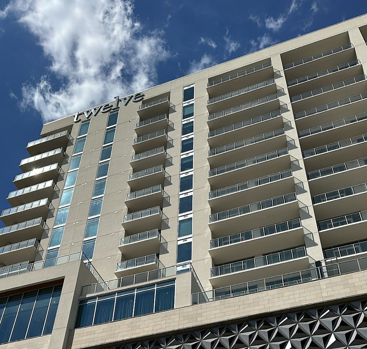Tall beige building with balconies against a blue sky with clouds; 