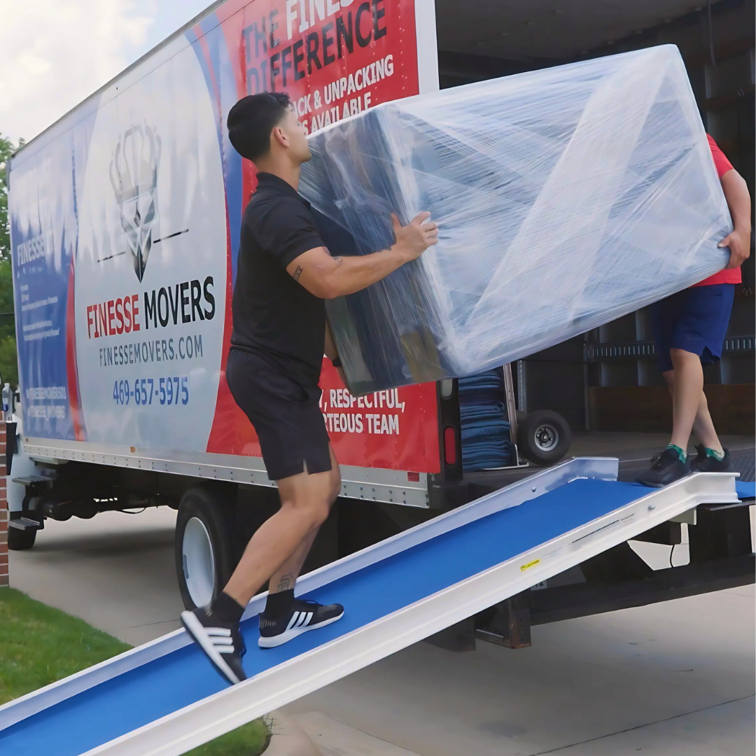 Movers loading a large, wrapped object onto a truck with a ramp.