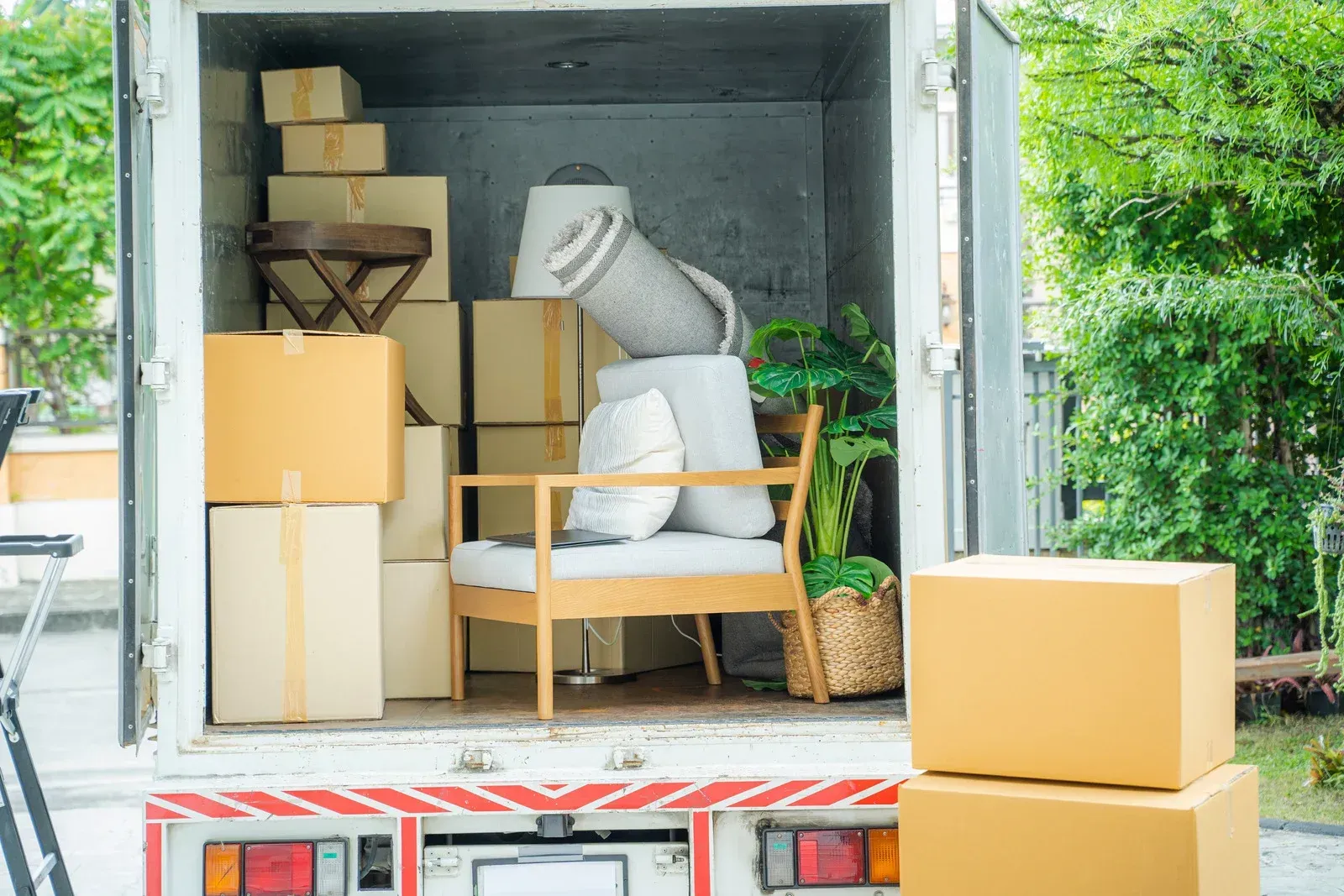 Truck bed loaded with cardboard boxes, a chair, lamp, and plant, ready for a move.