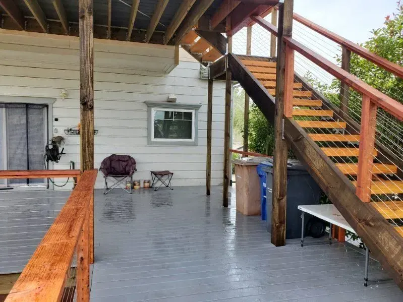 Wooden deck and stairs.  Gray painted floor, light-colored siding, and a window.