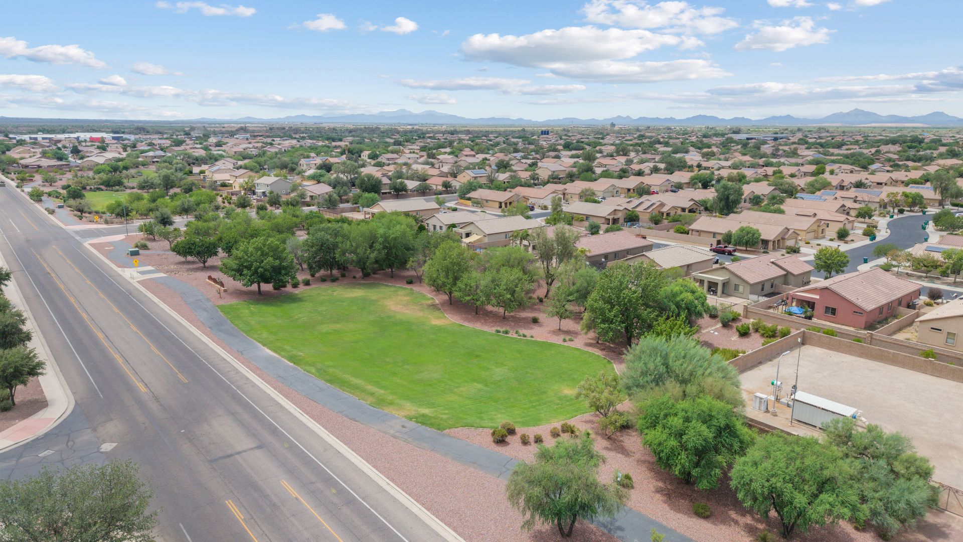 Aerial view of a suburban neighborhood with houses, road, and a green field. Blue sky with clouds.