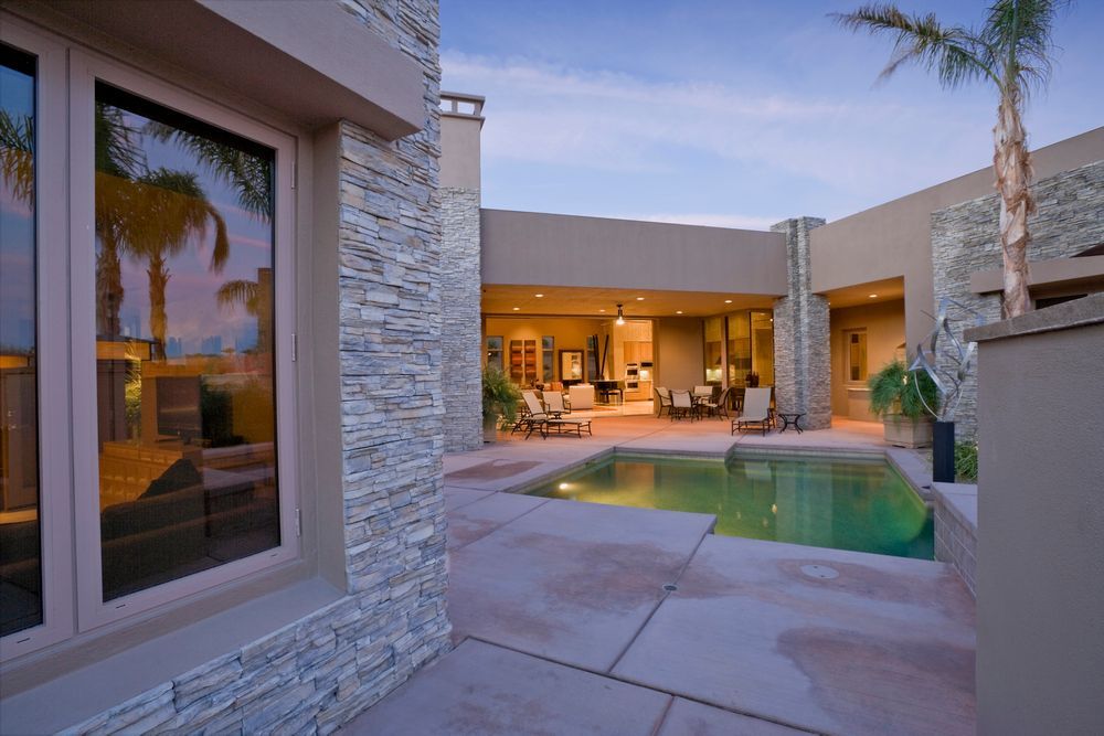 Courtyard with a pool, surrounded by a modern home with stone accents and a palm tree.