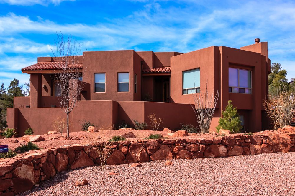 Red-brown stucco home with a terracotta tile roof and windows under a blue sky.