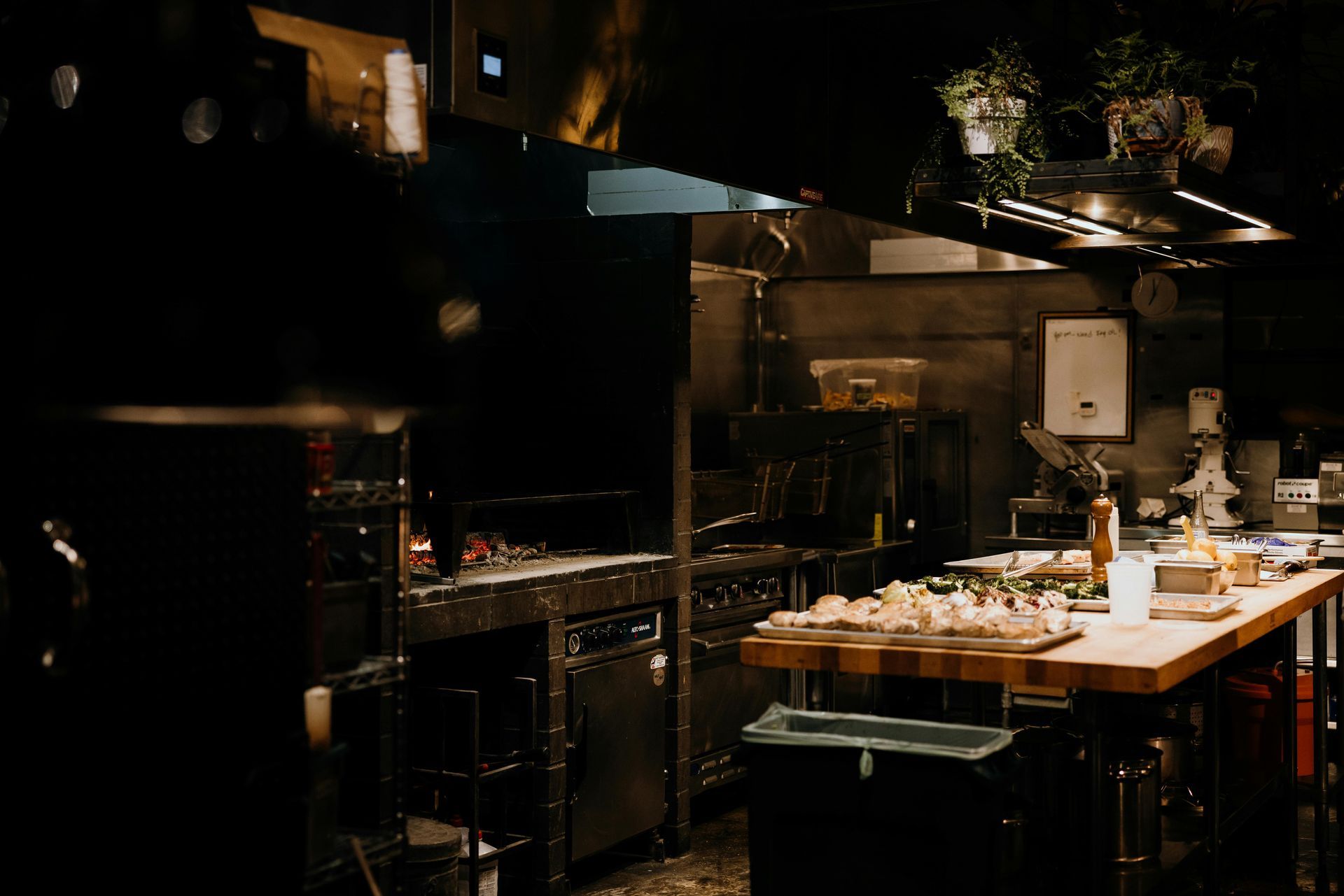 Dark commercial kitchen with a grill, cooking surfaces, and food preparation area.