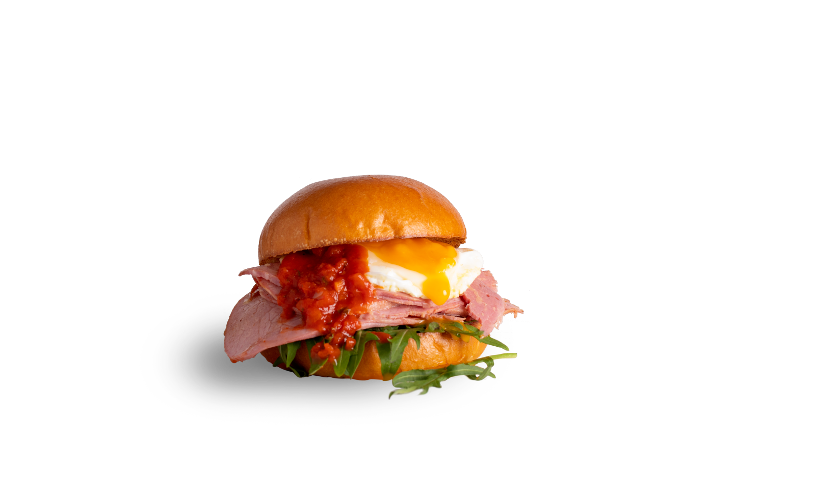 A breakfast sandwich on a brioche bun with sliced ham, a sunny-side-up egg, red relish, and fresh arugula.