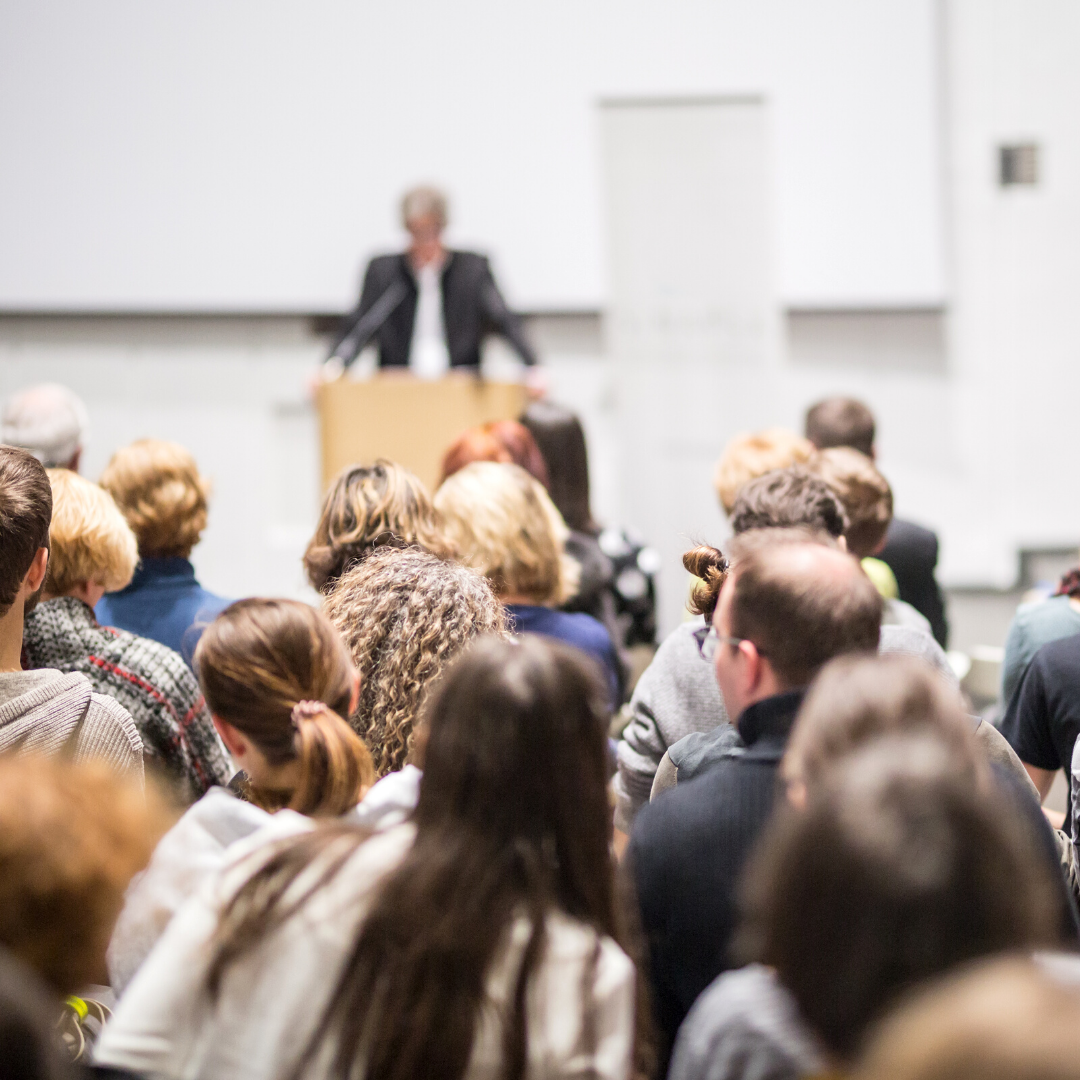 A speaker stands at a podium in a lecture hall before a seated audience.