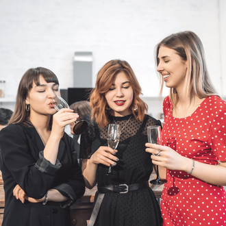 Three people stand in a room, holding champagne flutes and smiling while socializing.