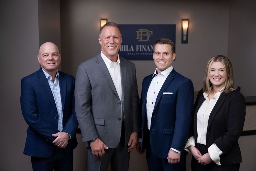 Four professionals posing in business attire in an office lobby, standing before a company sign.