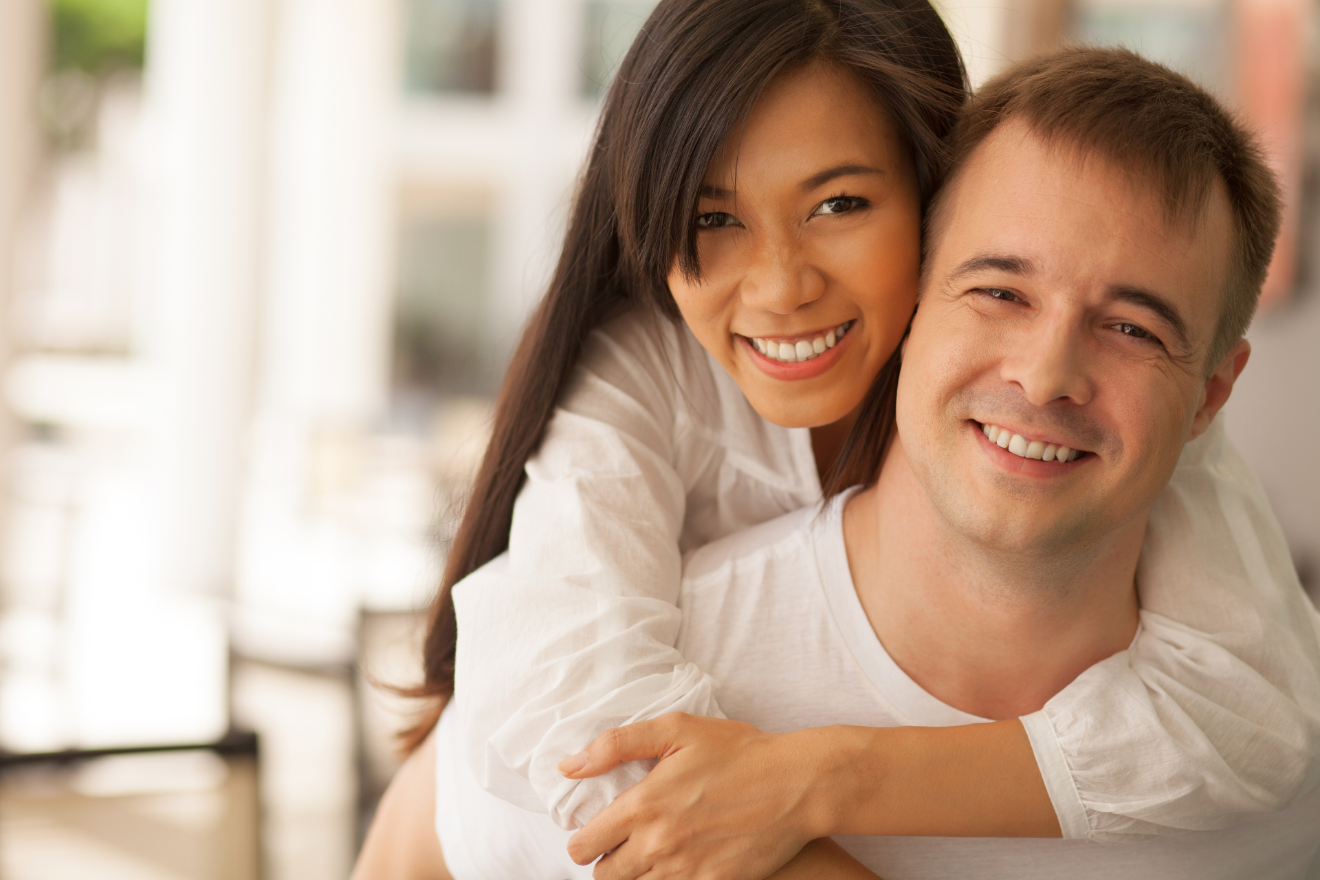 Smiling couple hugging indoors, with the woman leaning over the man's shoulders