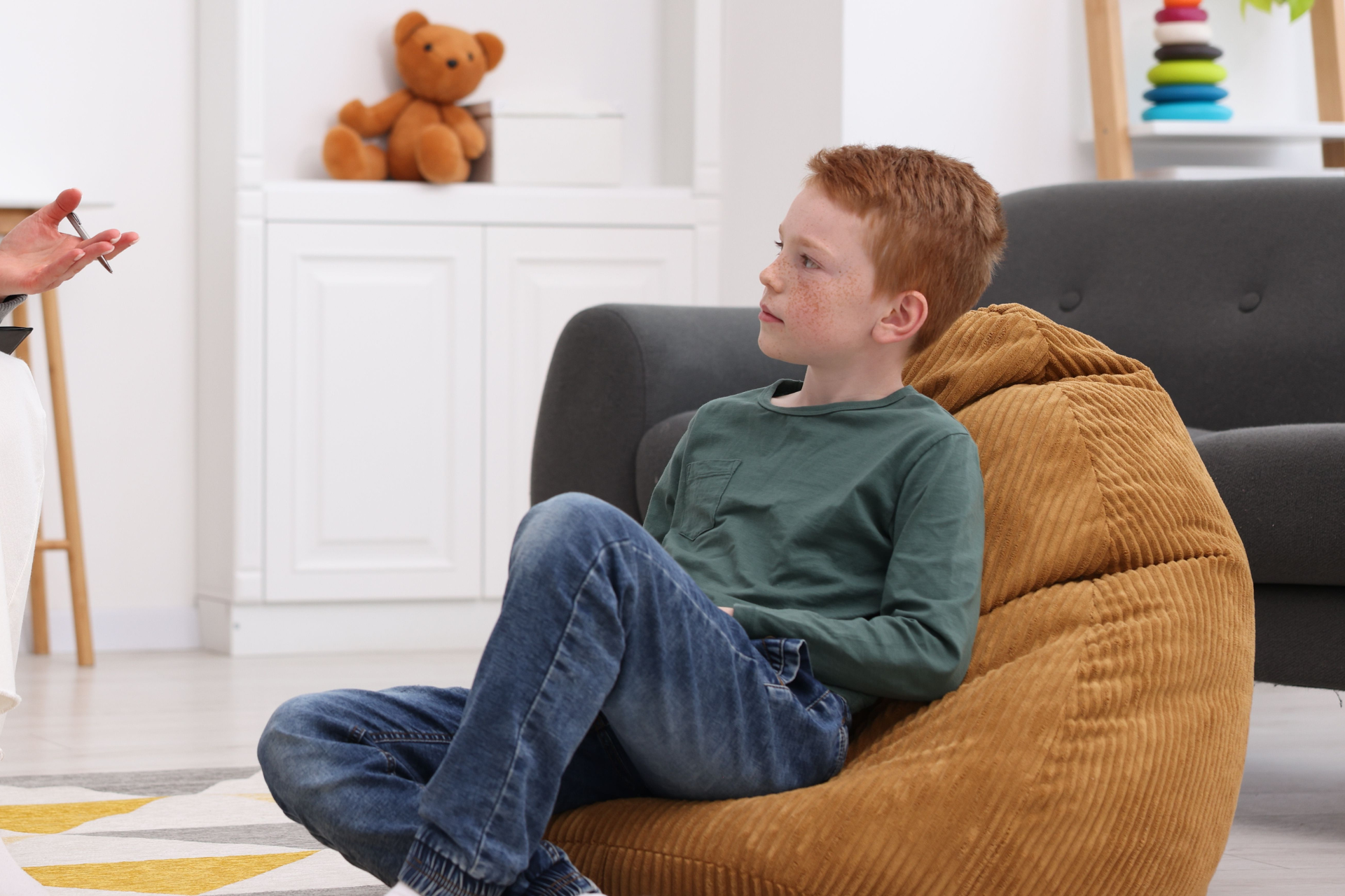 Child sitting on a brown bean bag chair in a bright living room, looking to the side
