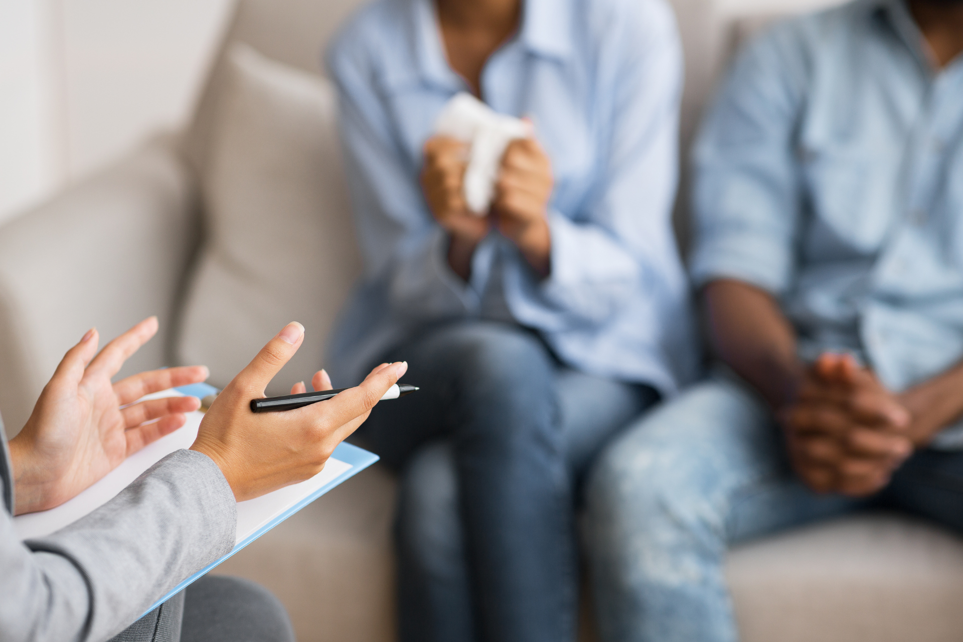 Person gesturing during a counseling session with two seated listeners on a couch
