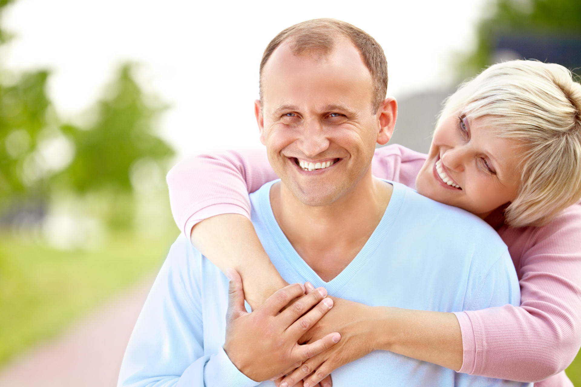 Smiling couple embracing outdoors on a sunny path, with greenery in the background