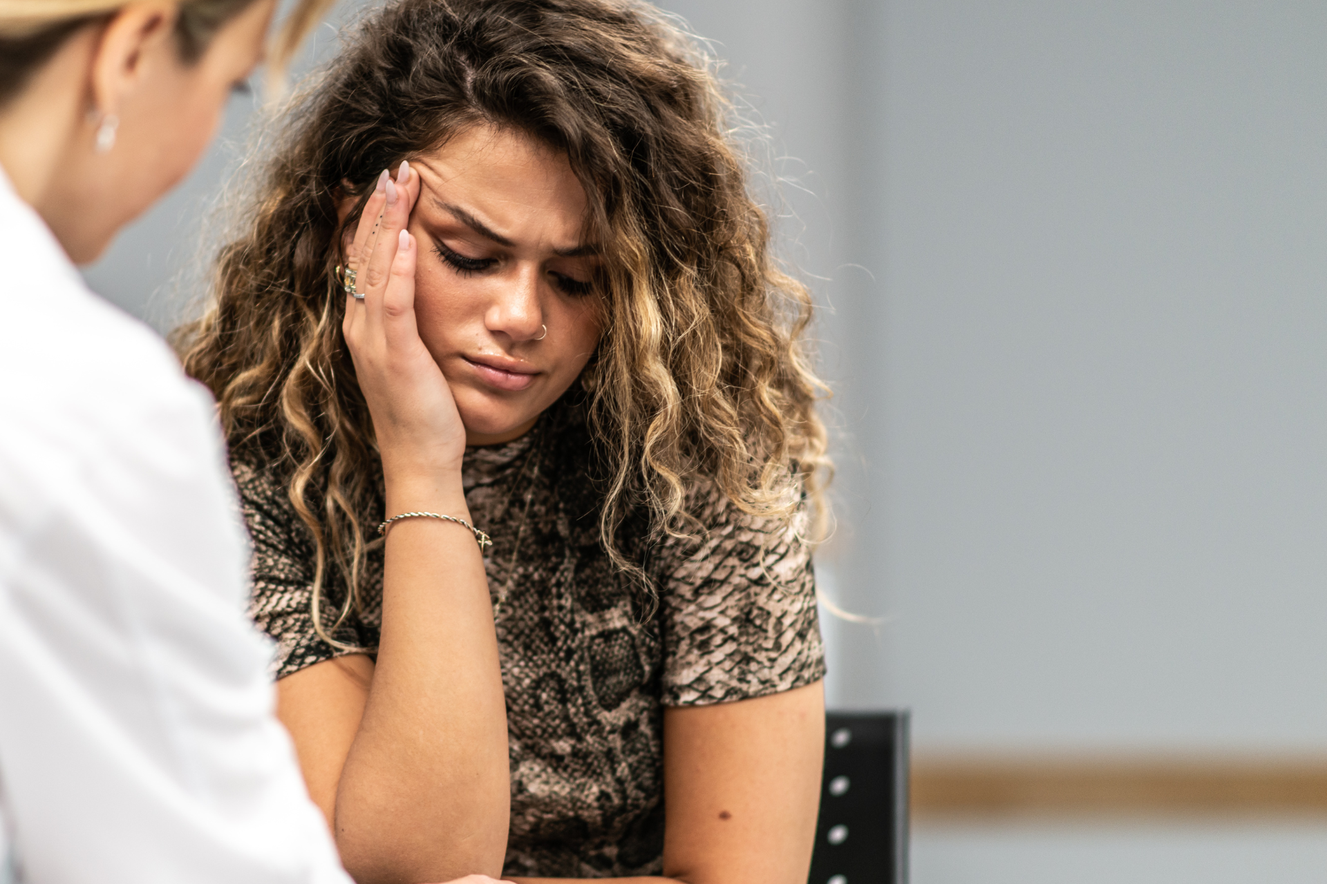 A woman sits with eyes closed while a man in a white coat holds her face in a counseling setting.
