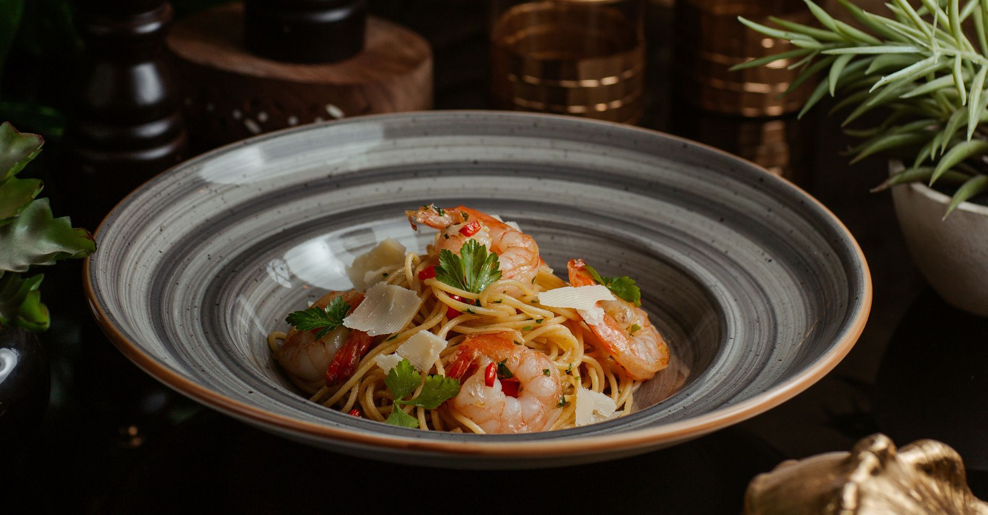 Spaghetti with shrimp in a gray and brown striped bowl, garnished with parsley and cheese.
