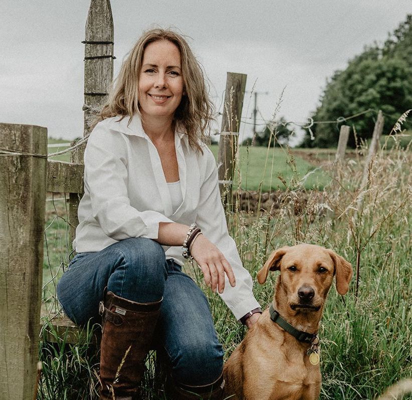 A woman is sitting next to a brown dog in a field