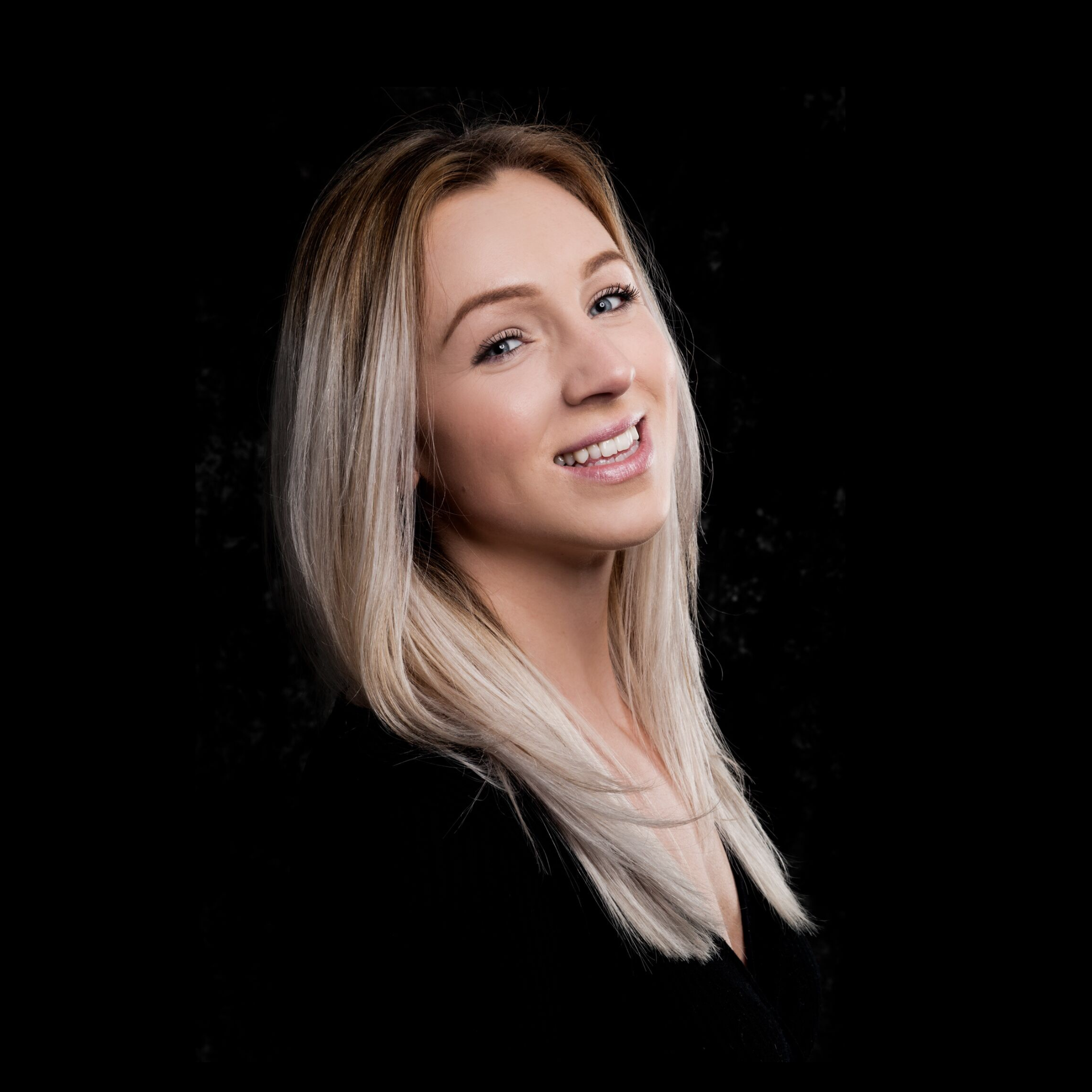 A woman with blonde hair is smiling in front of a black background.