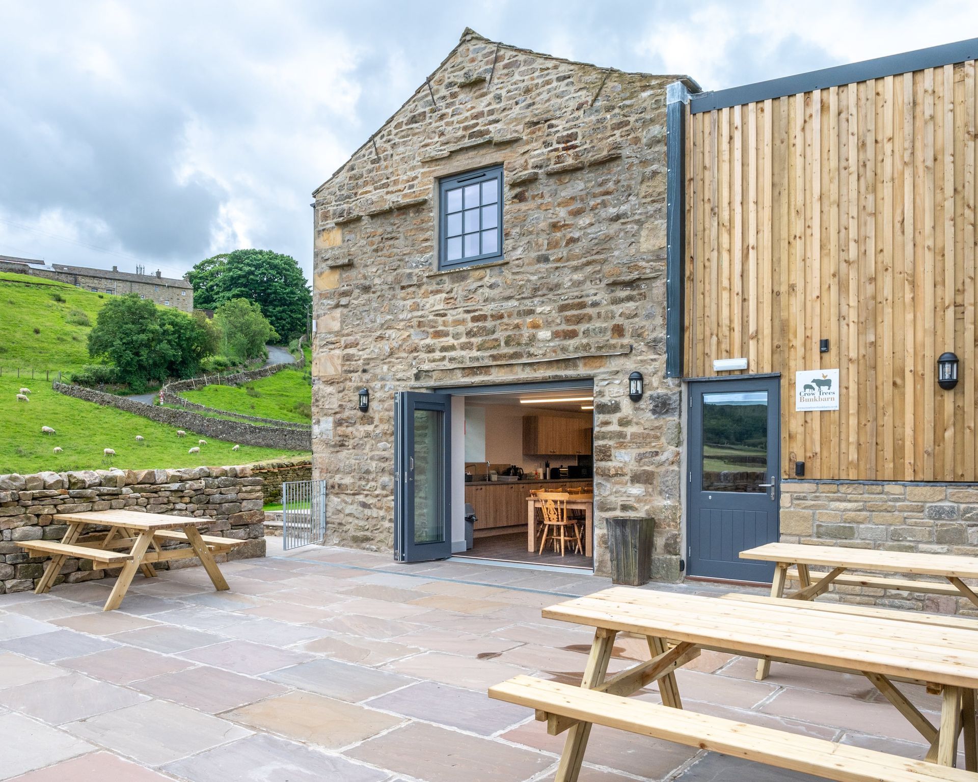 A brick building with a wooden roof and a patio with wooden picnic tables in front of it.