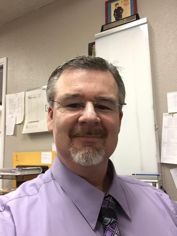 A man in a purple shirt and tie is smiling for the camera