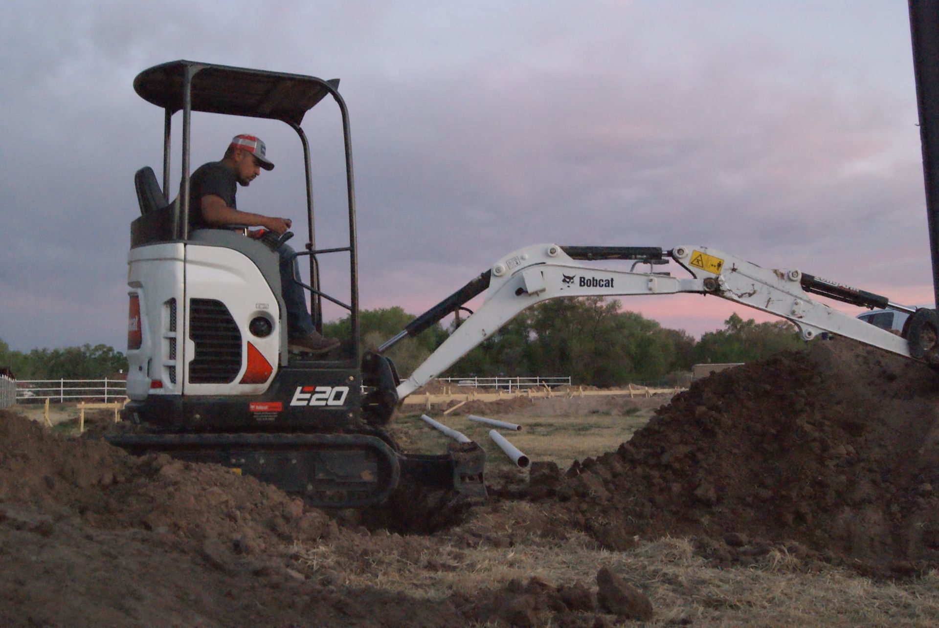 A man is driving a bobcat excavator in a dirt field