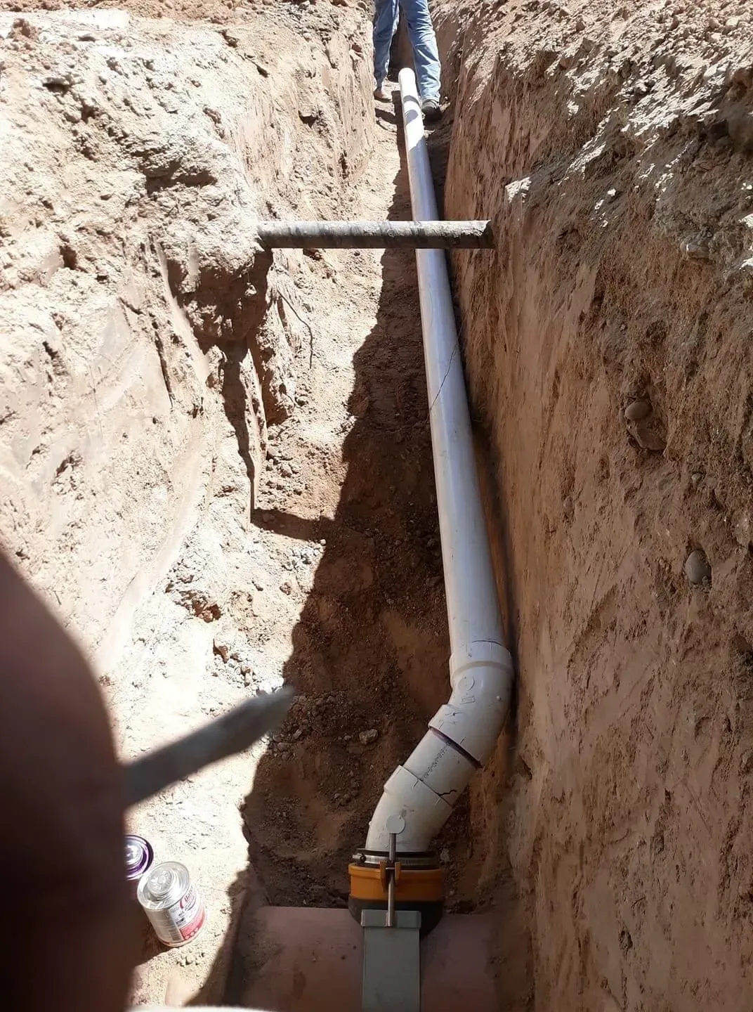 A white pipe is being installed in a trench