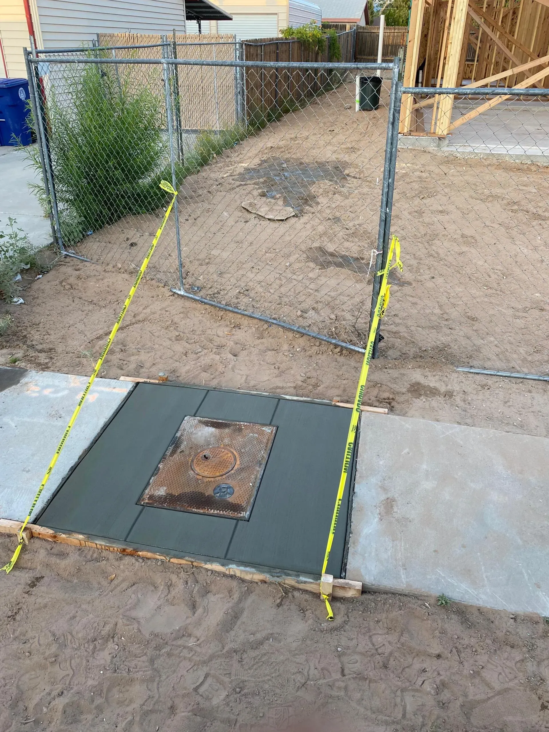A manhole cover is sitting on top of a concrete slab next to a fence.