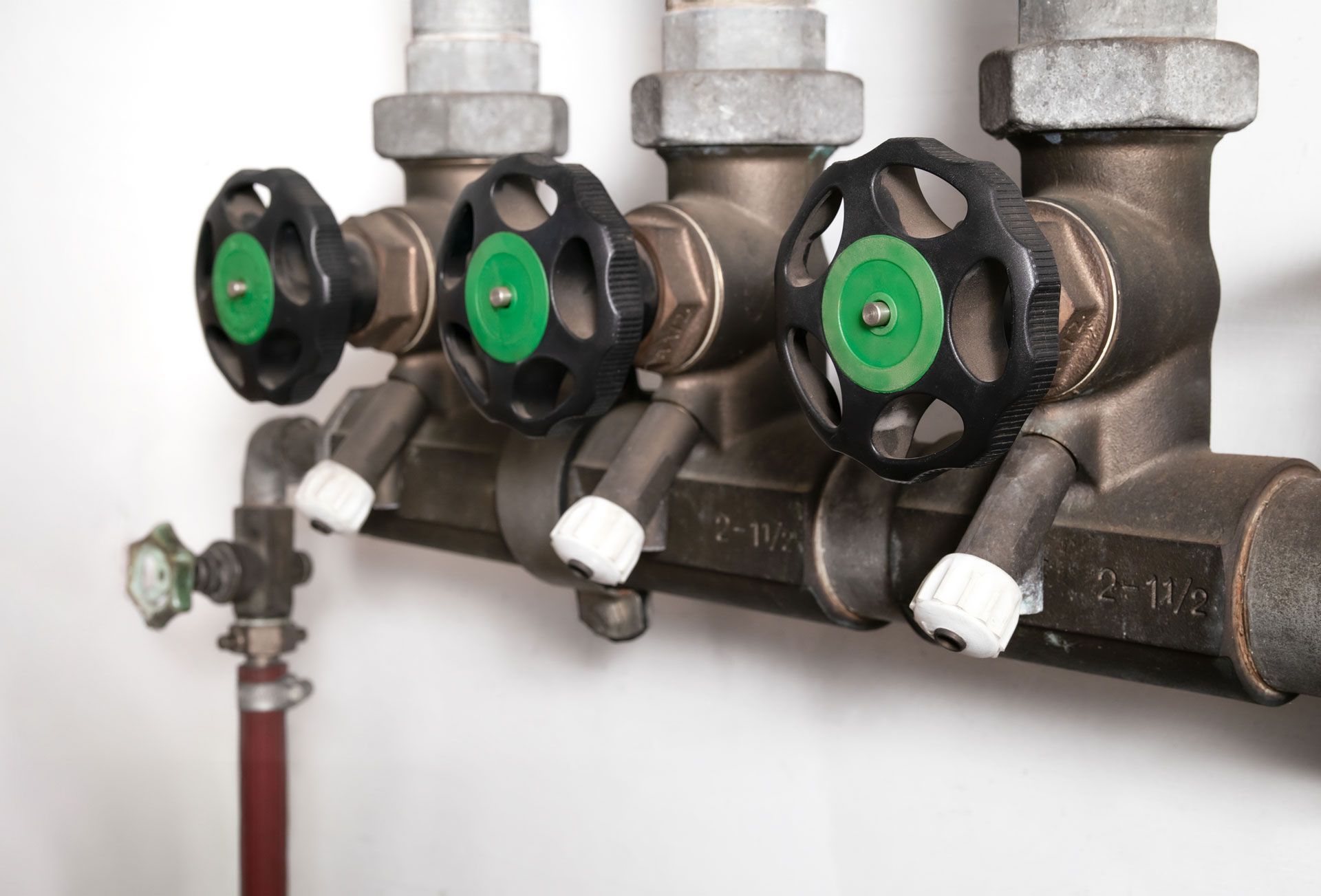Close-up of plumbing manifold valves with black bodies and green adjustment knobs on metal pipes.
