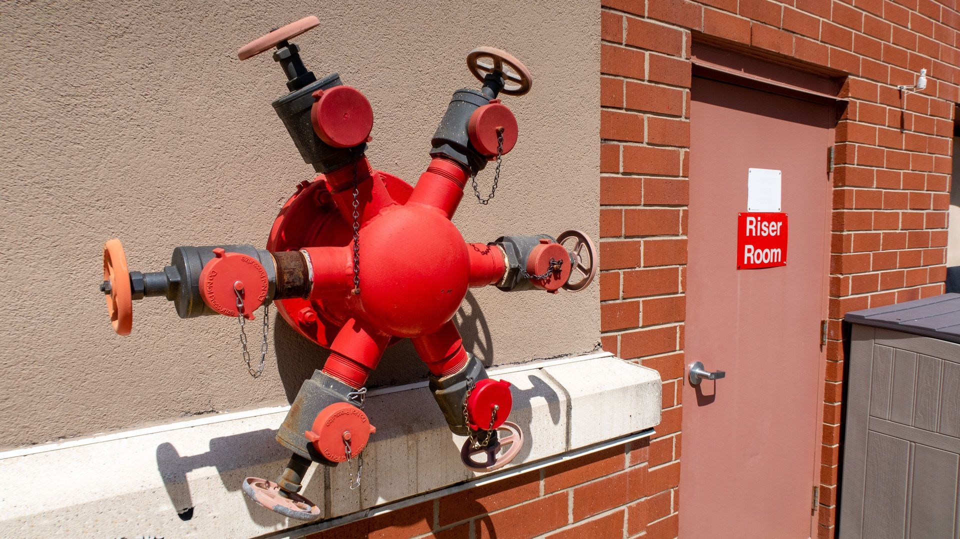Red fire hydrant sculpture mounted on a brick wall beside a door labeled “Fire Room.”