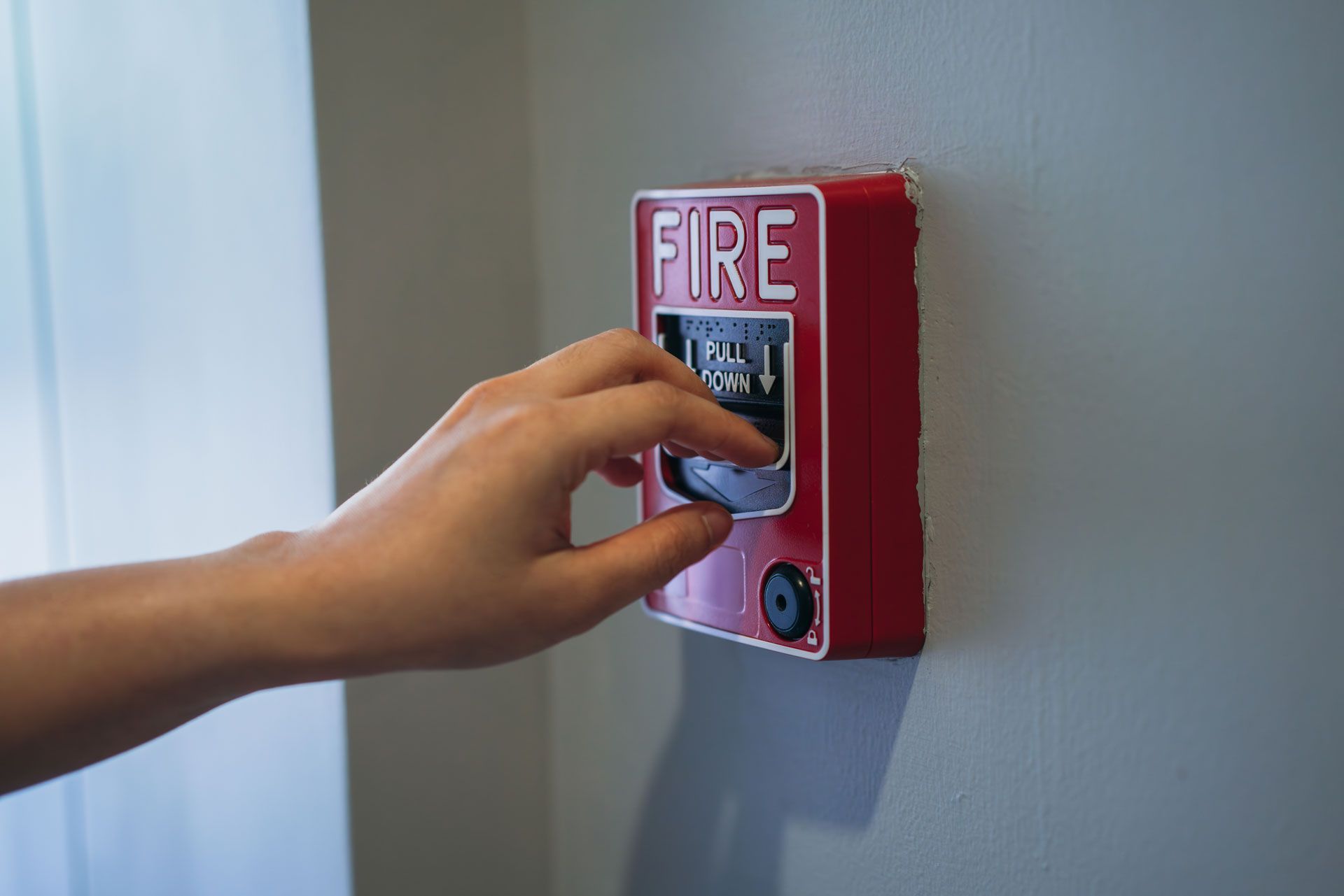 Hand pressing a red fire alarm pull station mounted on a wall